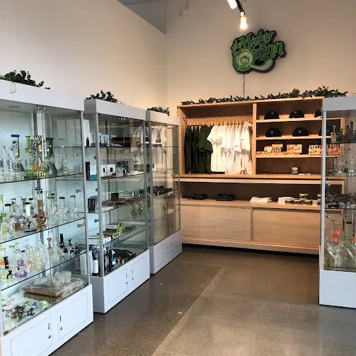 Glass cabinets filled with glassware, accessories, and smoking tools in Cannavine Ukiah. A wooden shelving unit in the back displays apparel, hats, and other branded merchandise beneath a "Muddy Green" neon-style sign.