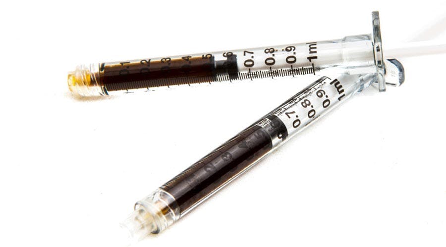 Two syringes filled with dark cannabis oil concentrate on a white background for medical or therapeutic use