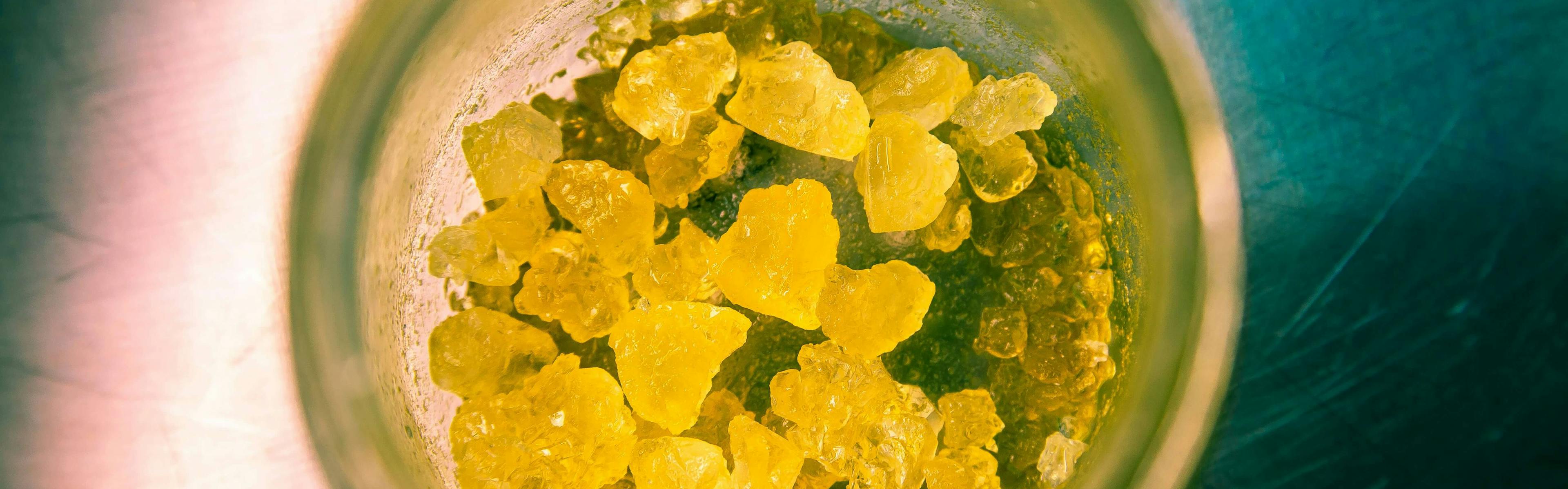 Jar filled with yellow THC-A crystals or cannabis diamond concentrates on a metal surface