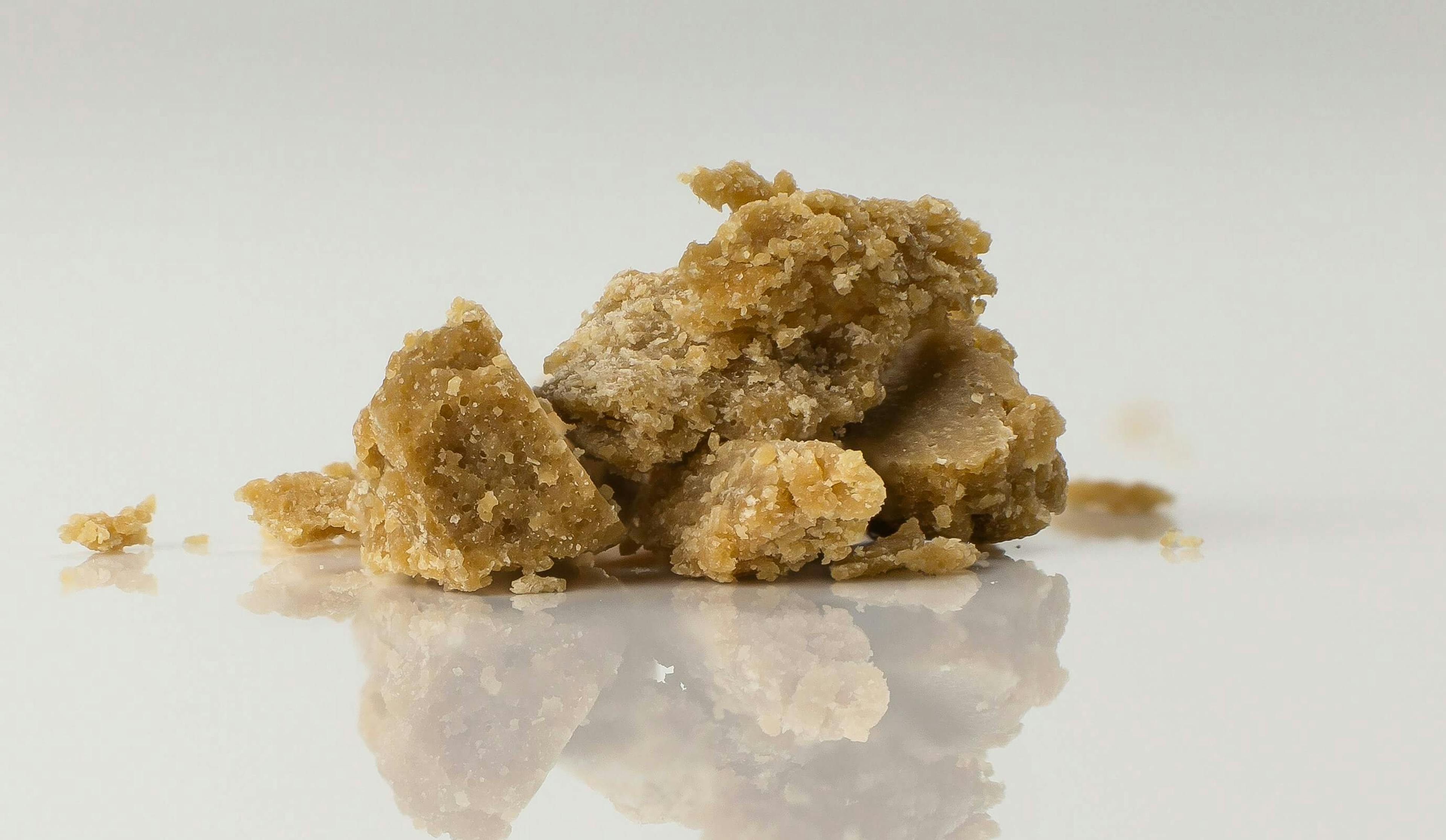 Close-up of crumbly brown cannabis concentrate, known as wax or crumble, on a reflective white surface