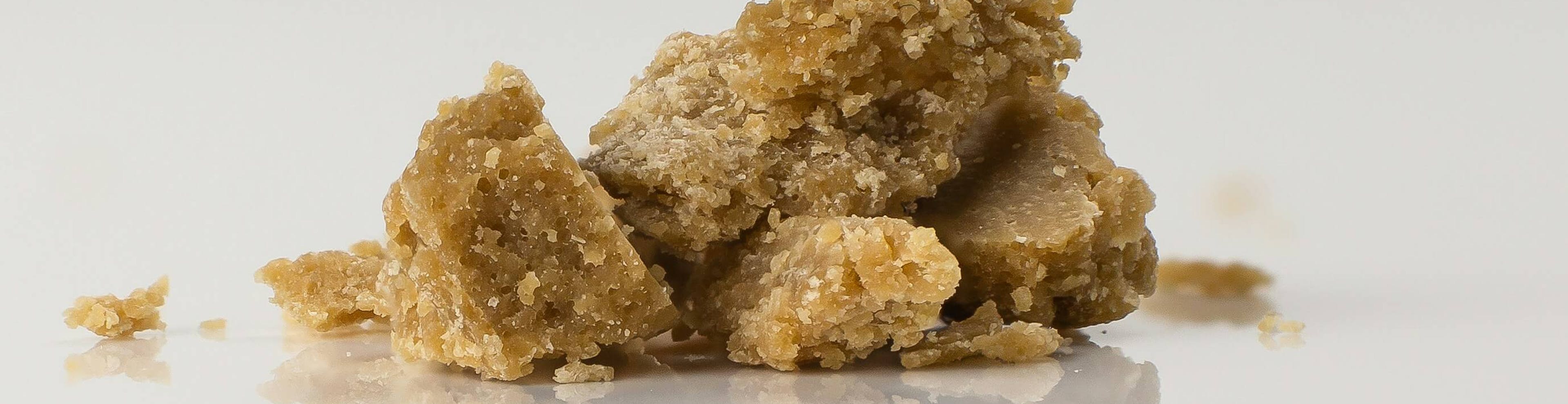 Close-up of crumbly brown cannabis concentrate, known as wax or crumble, on a reflective white surface