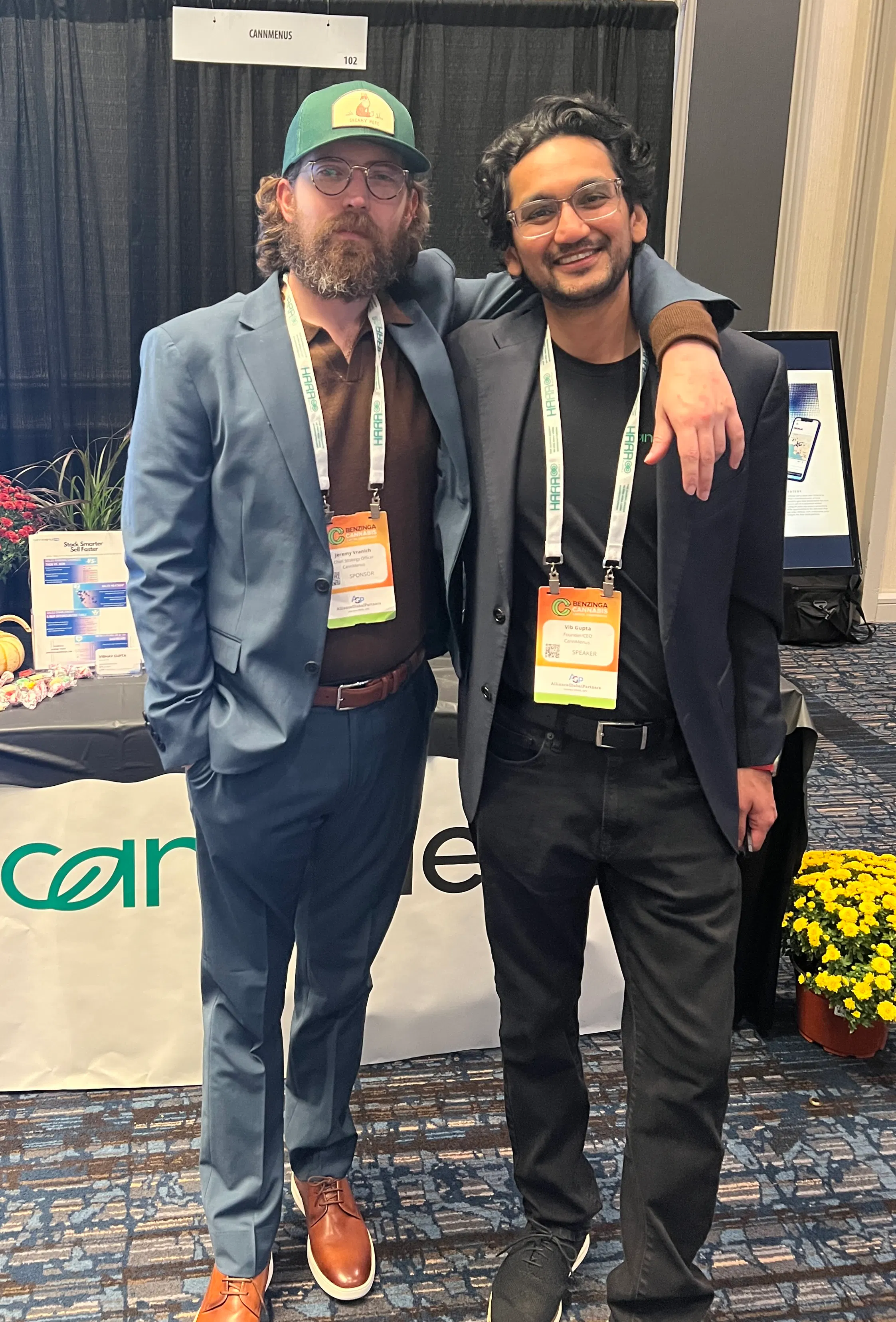 Two smiling individuals standing in front of the CannMenus booth at the Benzinga Cannabis Conference in Chicago.