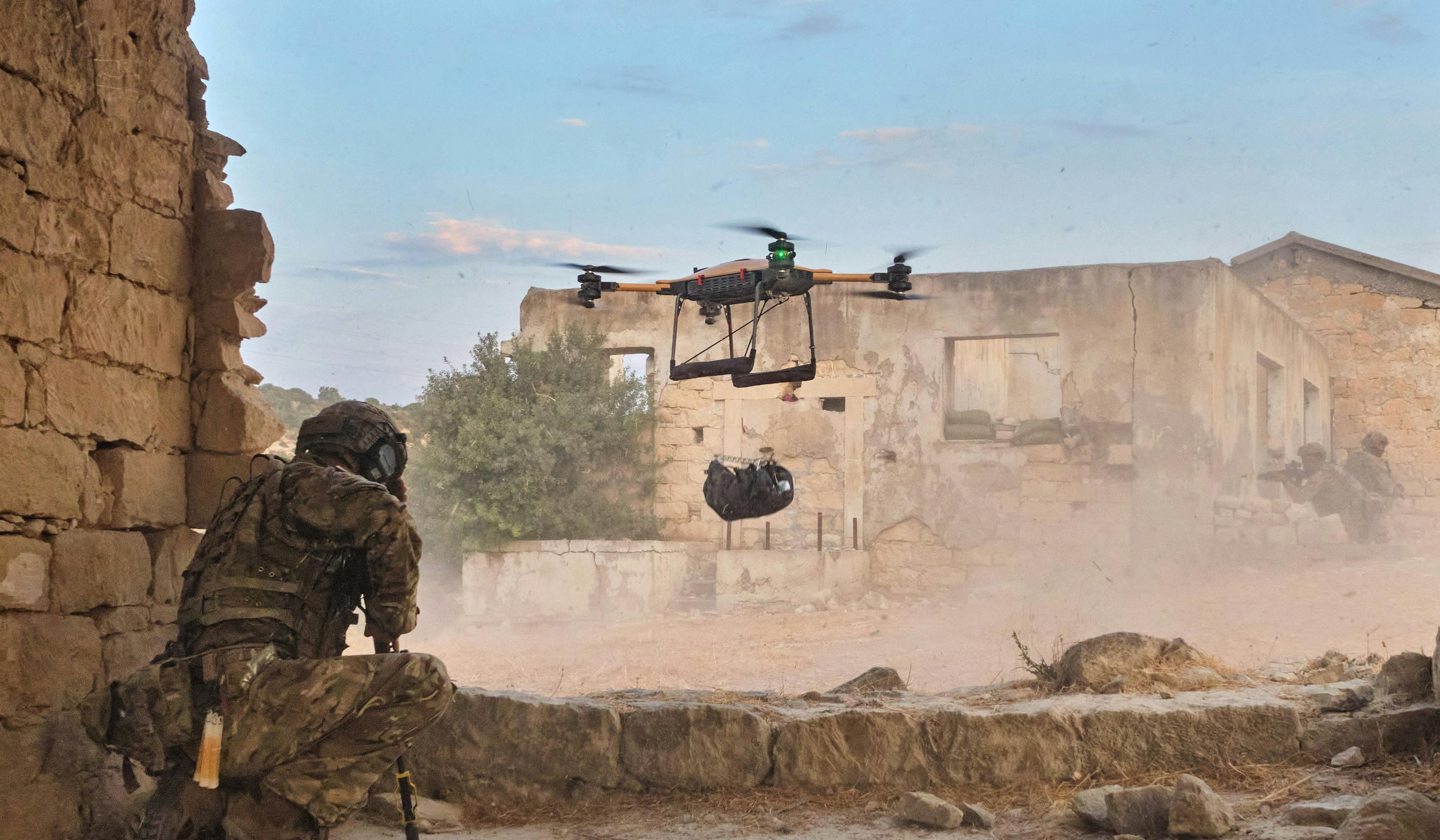A solider watching a drone carry equipment.