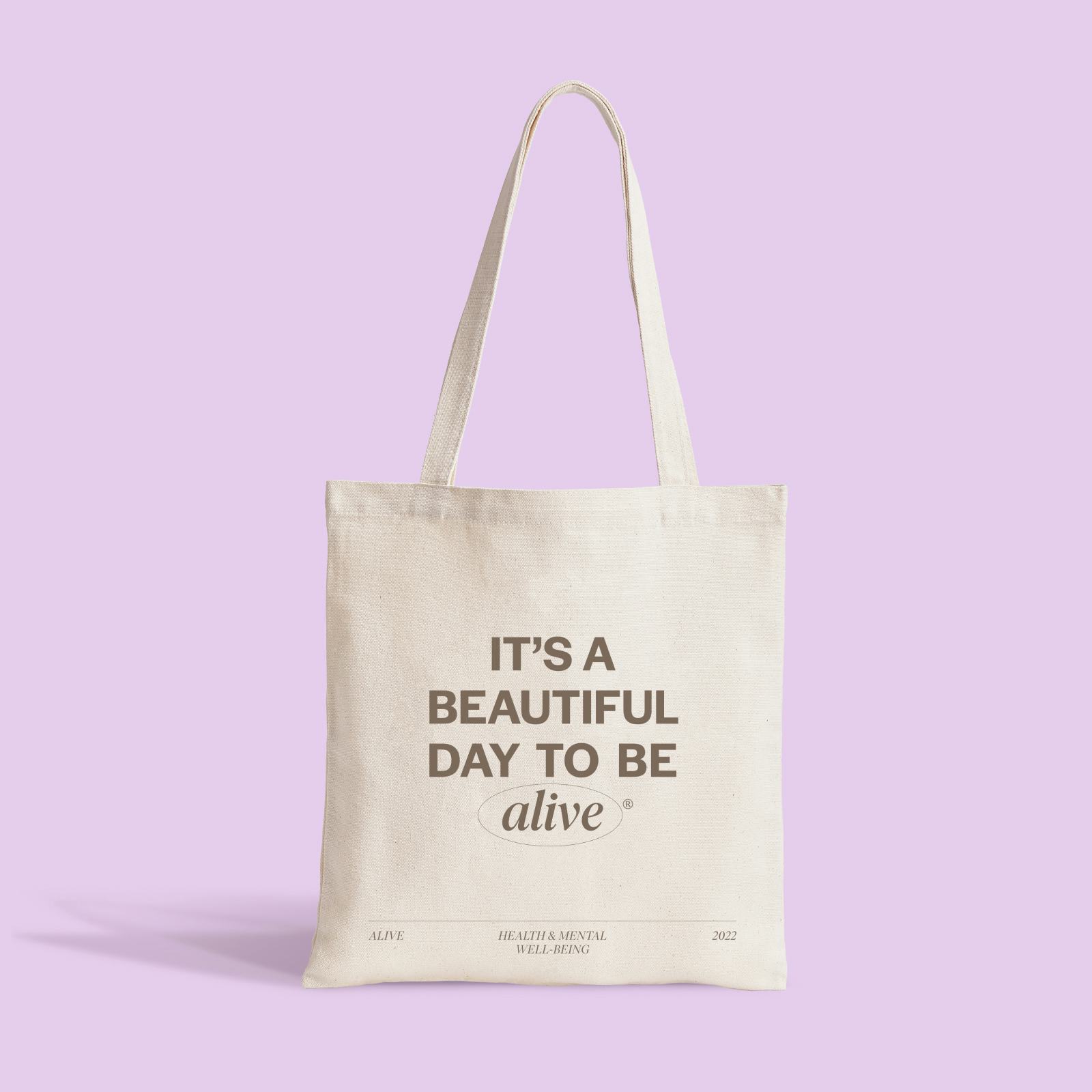 A tote bag with the text 'it's a beautiful day to be alive' against a pink background.