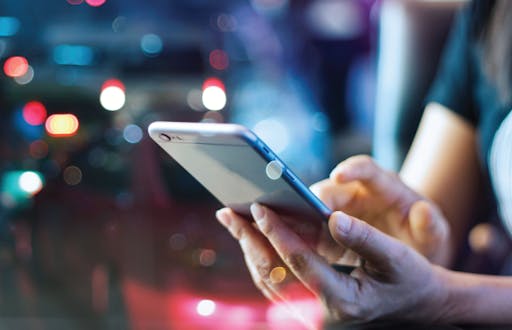 Cell phone being used against the backdrop of city lights at night.