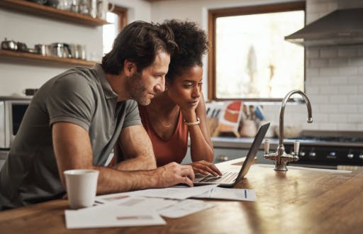Two people looking at a laptop on their kitchen counter.