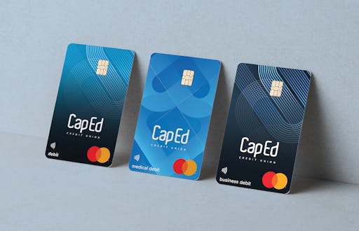 Three CapEd debit cards leaned against a wall. Each card features a different design with the CapEd and Mastercard logo.