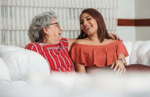Two women sitting next to each other on a couch laughing.