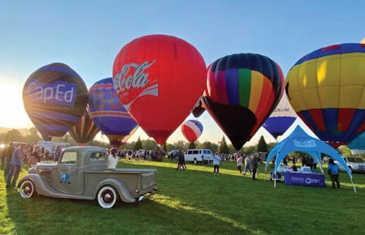 Several hot air balloons on the grass in Ann Morrison park. CapEd vintage truck and blue canopy in foreground of hot air balloons. 
