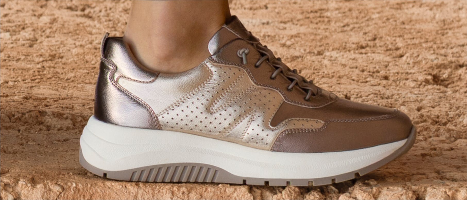 Woman wearing dark brown sneakers in front of a stone wall.