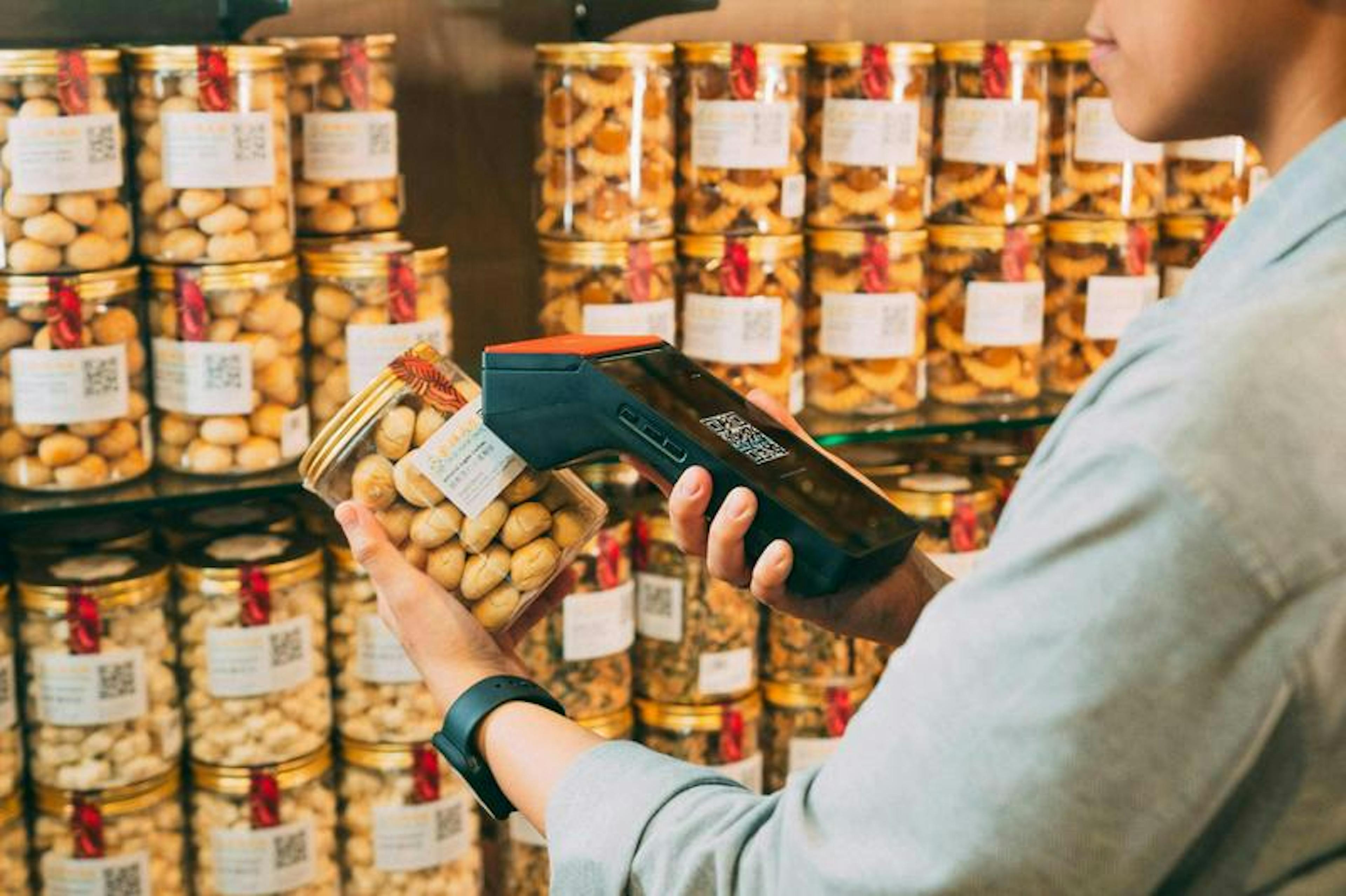 Person scans jar of snacks with barcode reader in store, surrounded by shelves filled with similar jars.