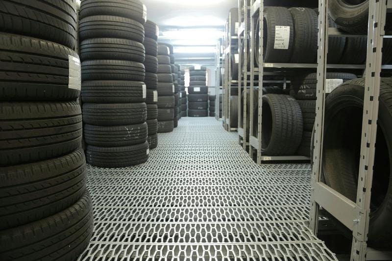 Neatly stacked tires on metal shelves create a walkway in a warehouse.