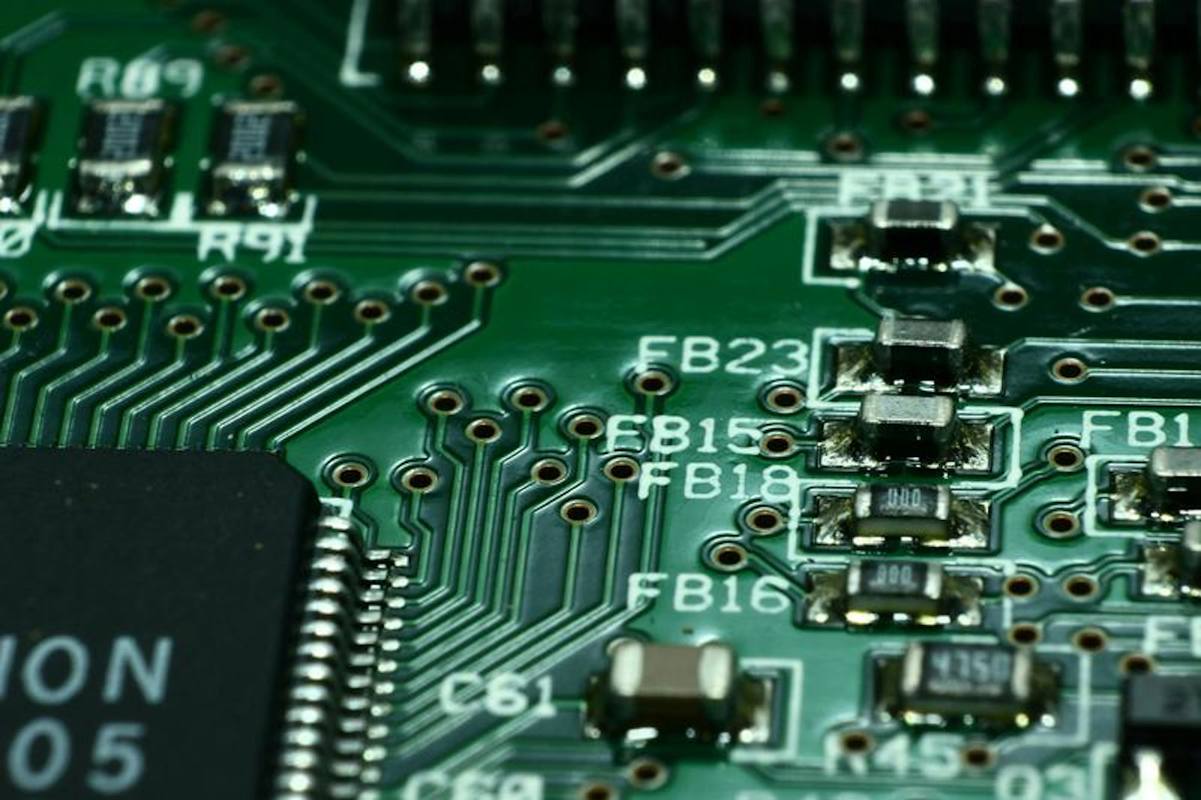 Green circuit board: microchips, pathways, labeled components like "FB15," "FB18," "FB23," "R9," and "4756."