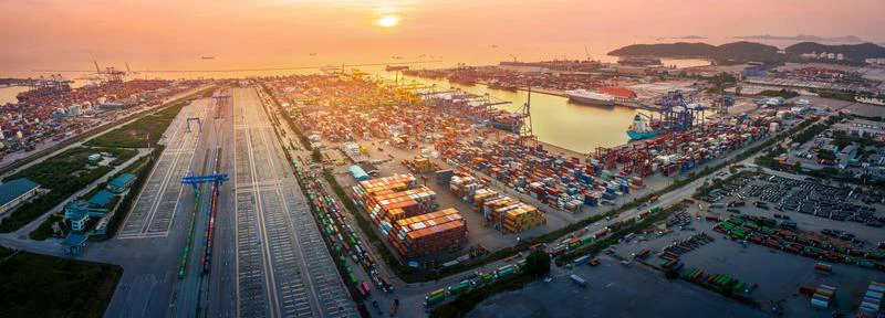 Containerterminals dicht aneinander, Kräne verladen Container. Sonnenuntergang beleuchtet Hafen, Schiffe im Wasser.