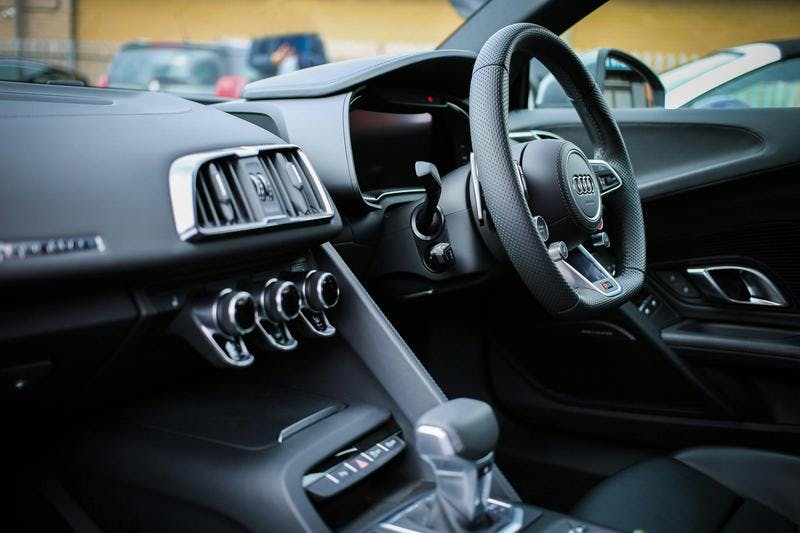 Sleek, modern car interior with Audi steering wheel, air vents, controls, gear shift, in parking lot.