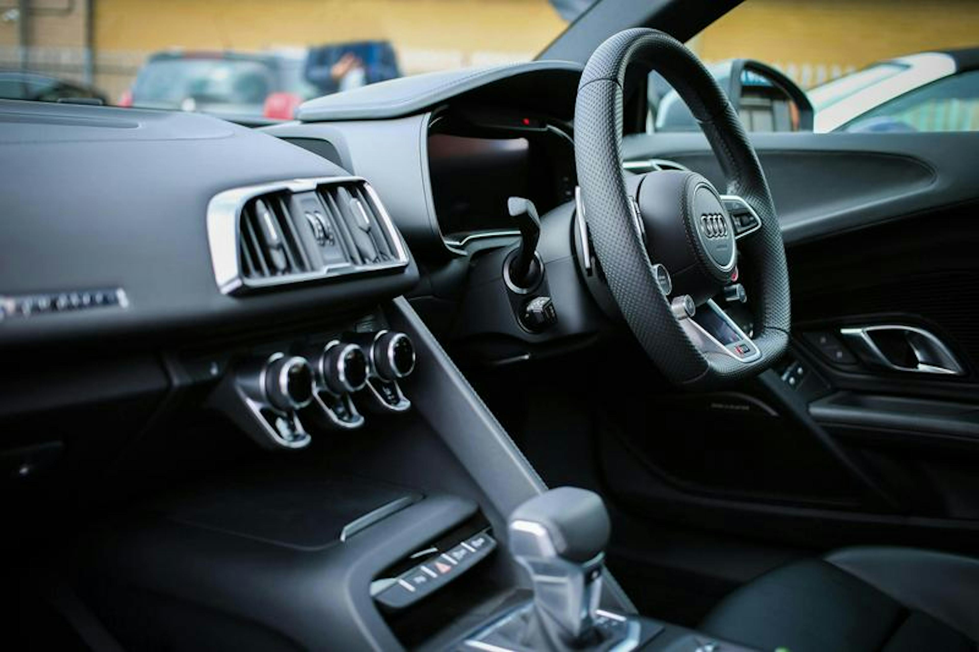 Sleek, modern car interior with Audi steering wheel, air vents, controls, gear shift, in parking lot.