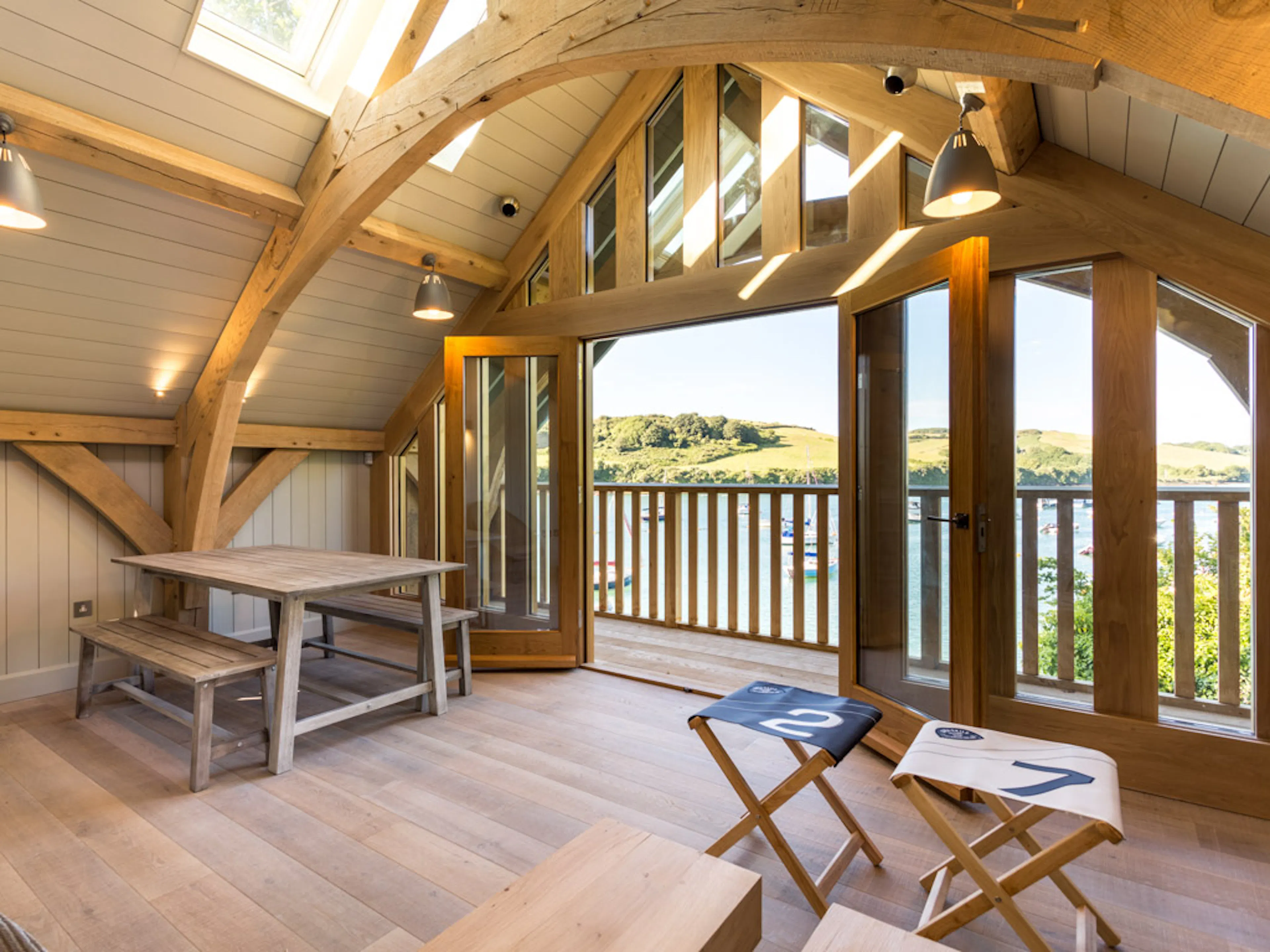 Interior view of a room within an oak framed boathouse with a timber balcony overlooking a river