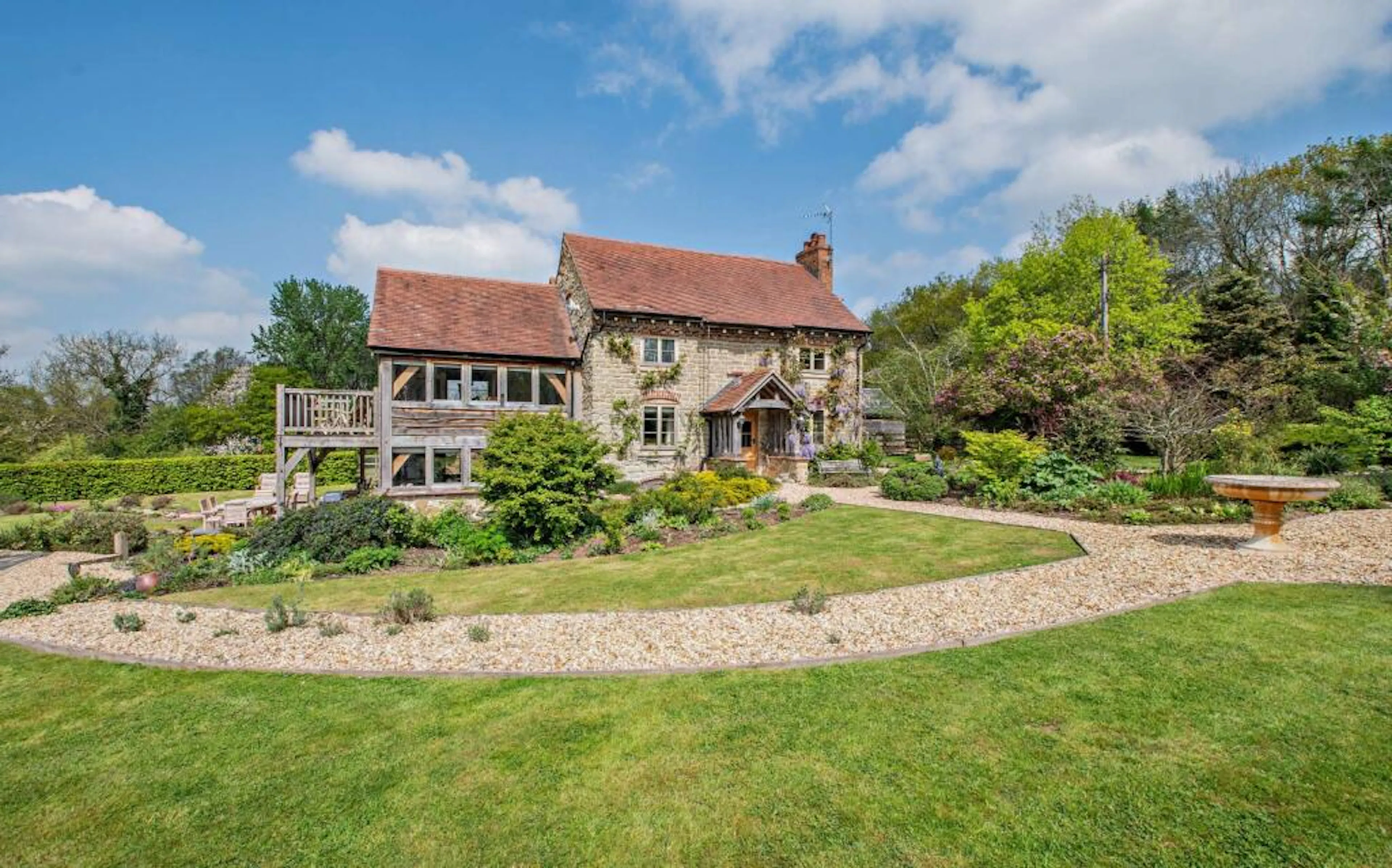 A landscaped garden in front of a traditional stone cottage with a red tile roof and oak framed extension