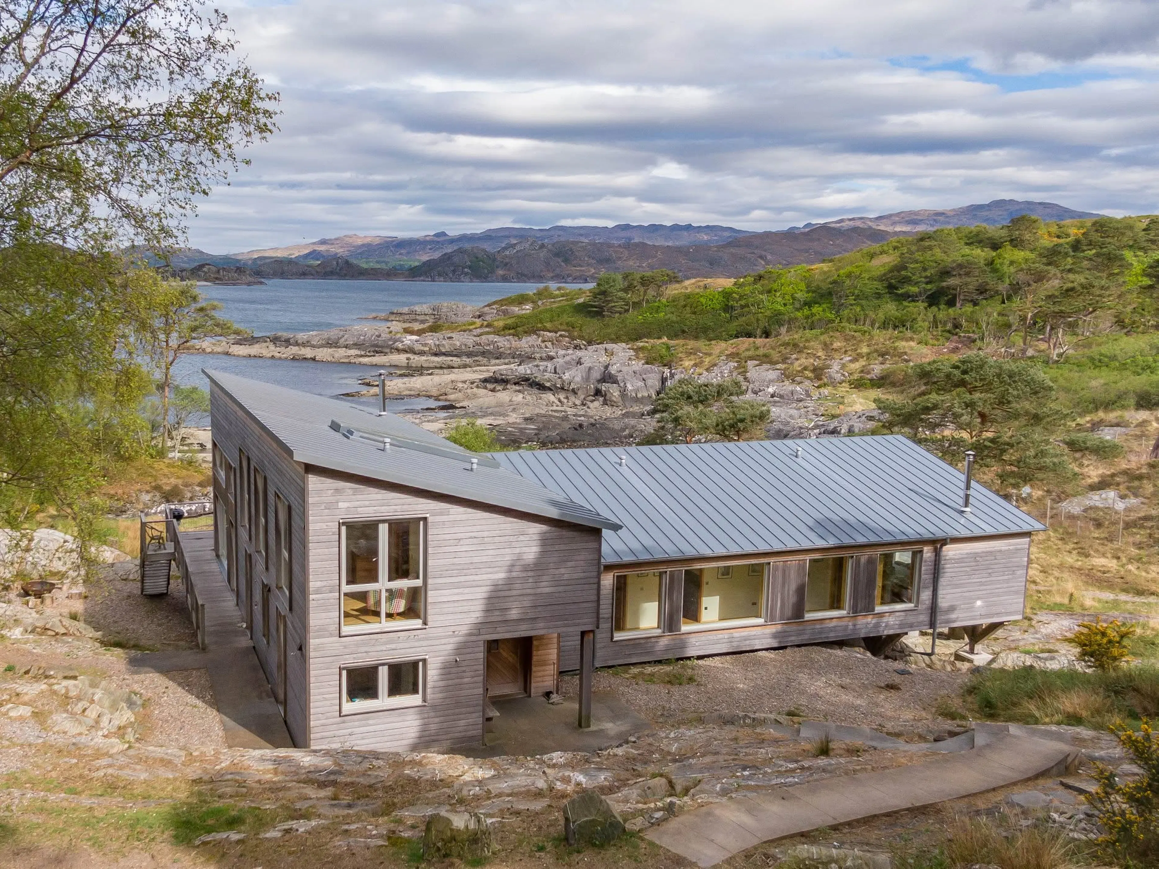 Exterior view of a timber clad Douglas fir framed house beside a loch with a rocky shoreline