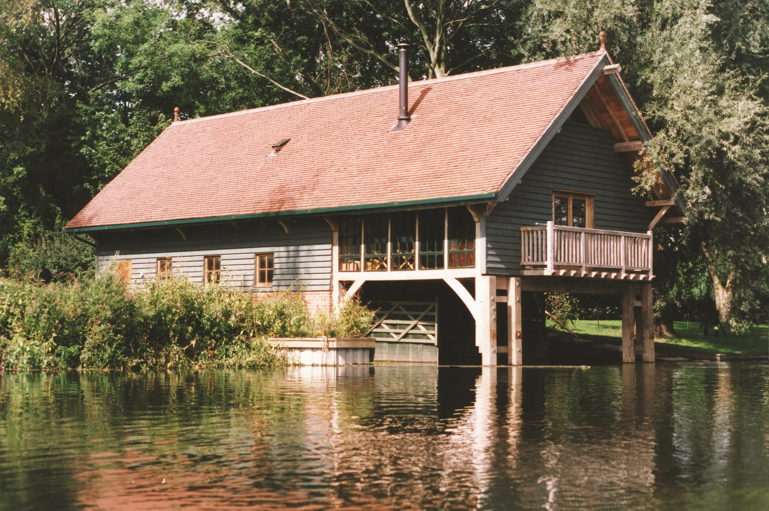 A red tiled oak framed boathouse with black horizontal cladding , which juts out over a lake