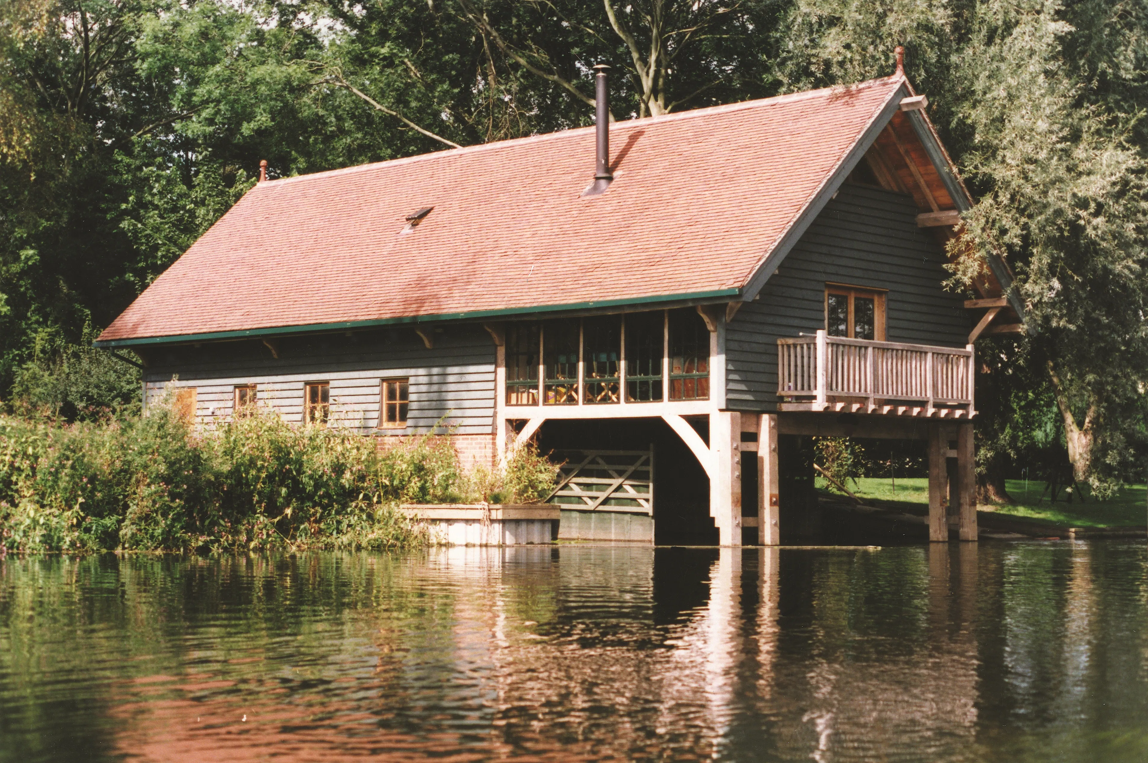 A red tiled oak framed boathouse with black horizontal cladding , which juts out over a lake 