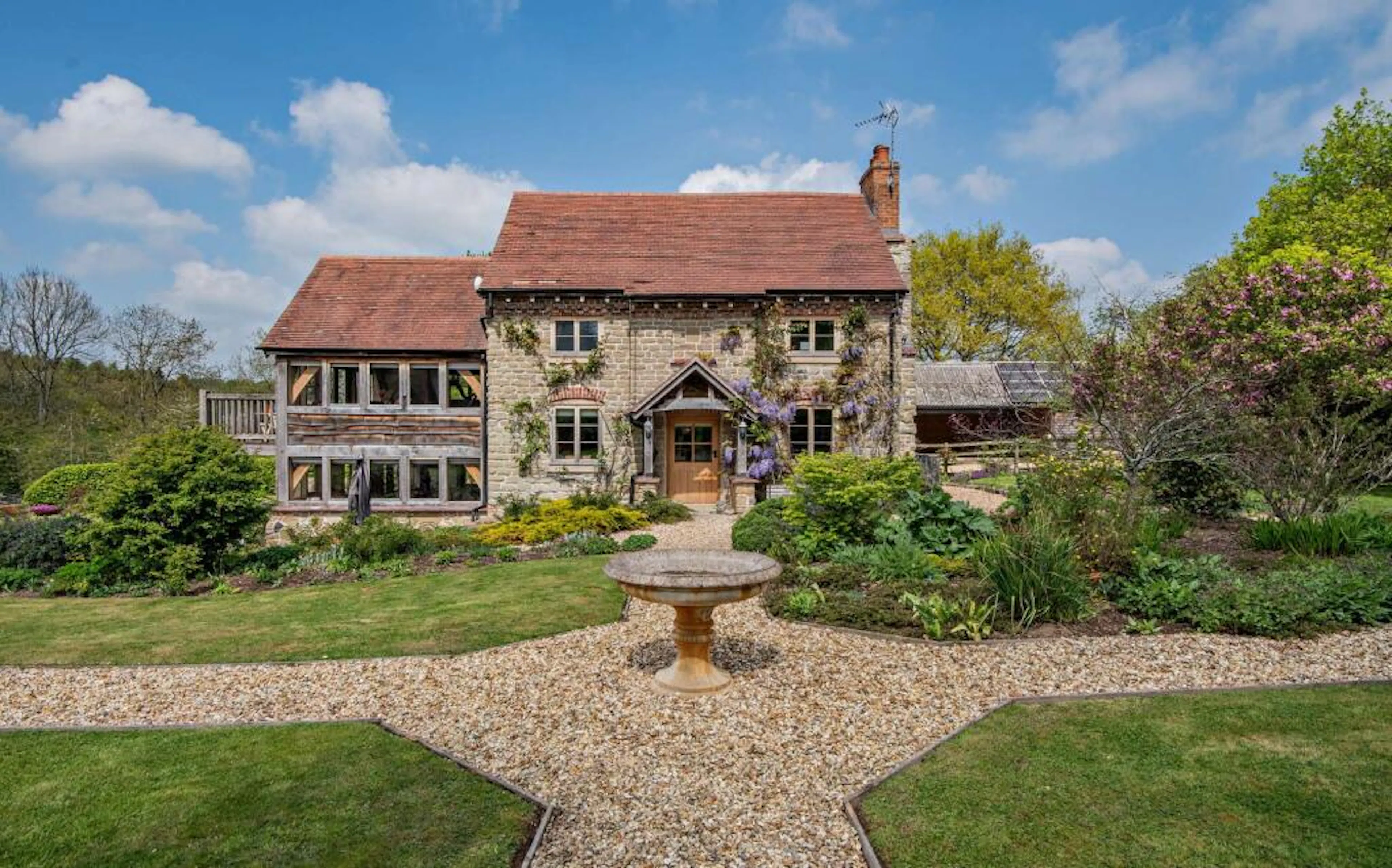 A landscaped garden in front of a traditional stone cottage with a red tile roof and oak framed extension