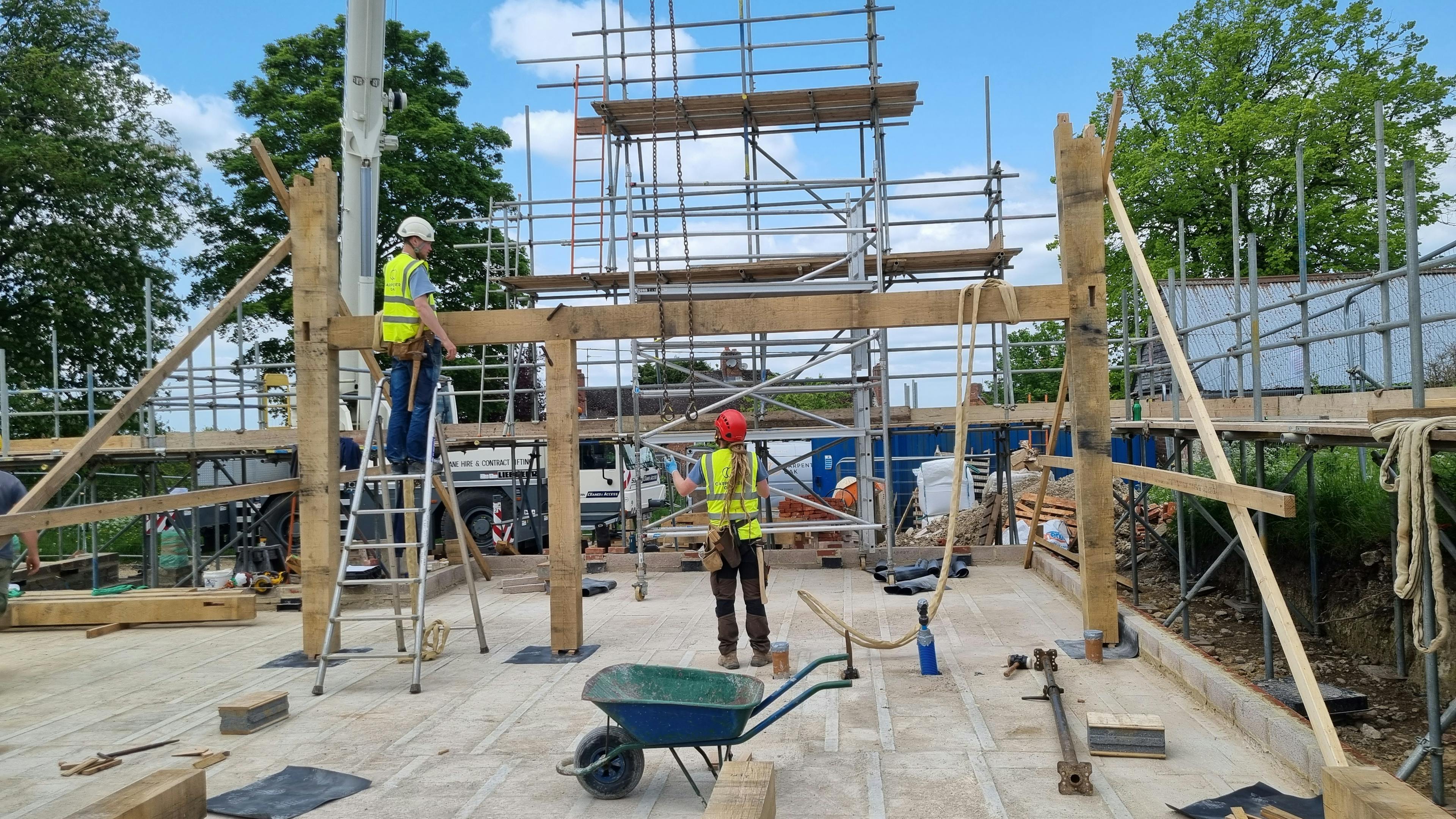 Carpenters on a building site in high vis jackets and hard hats during installation of an oak frame home