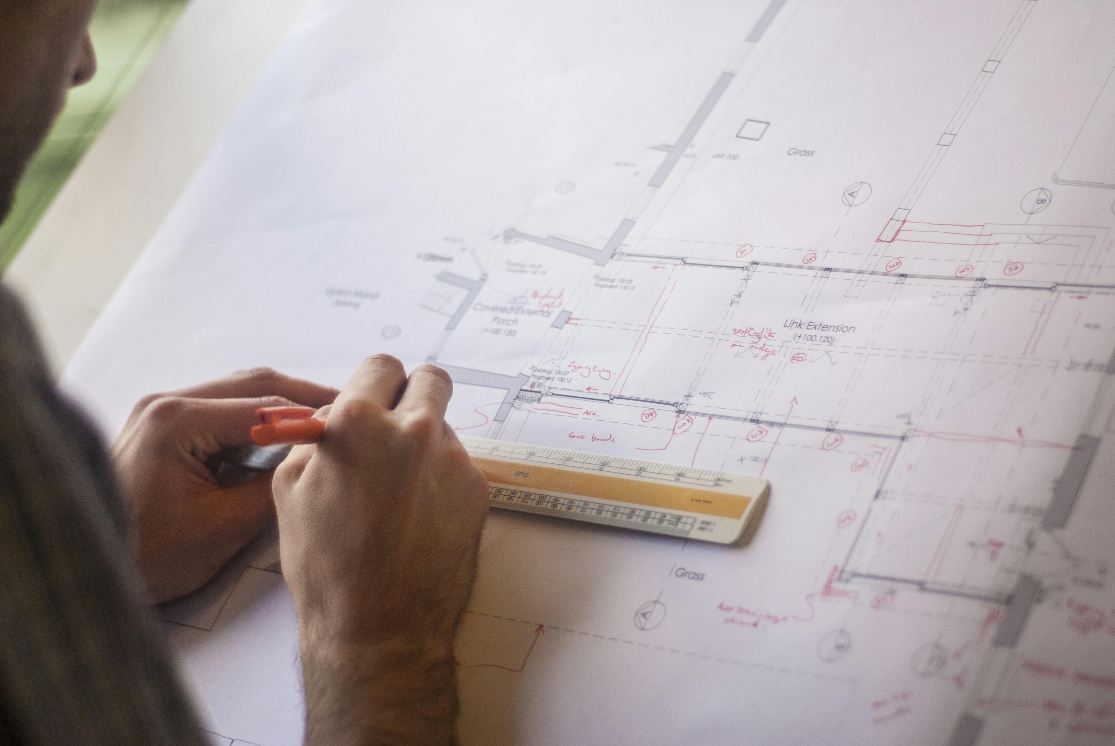 An architect with pen and ruler drawing on floorplans for a building
