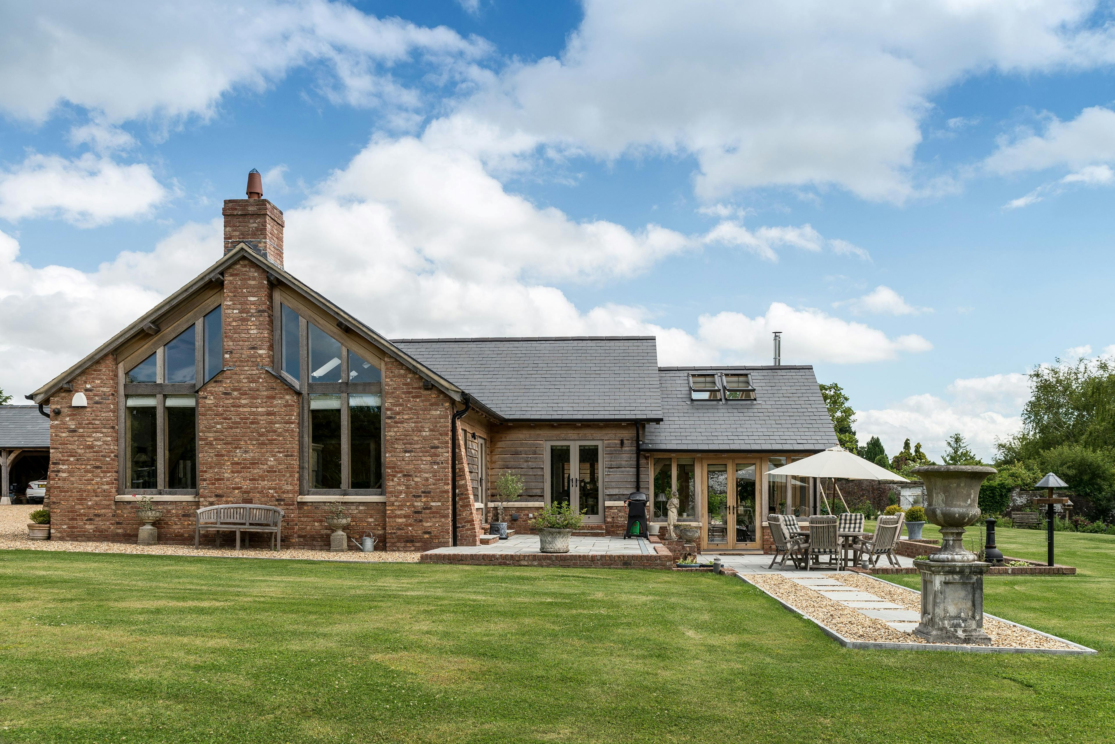 An oak framed barn home set in landscaped gardens with a green lawn