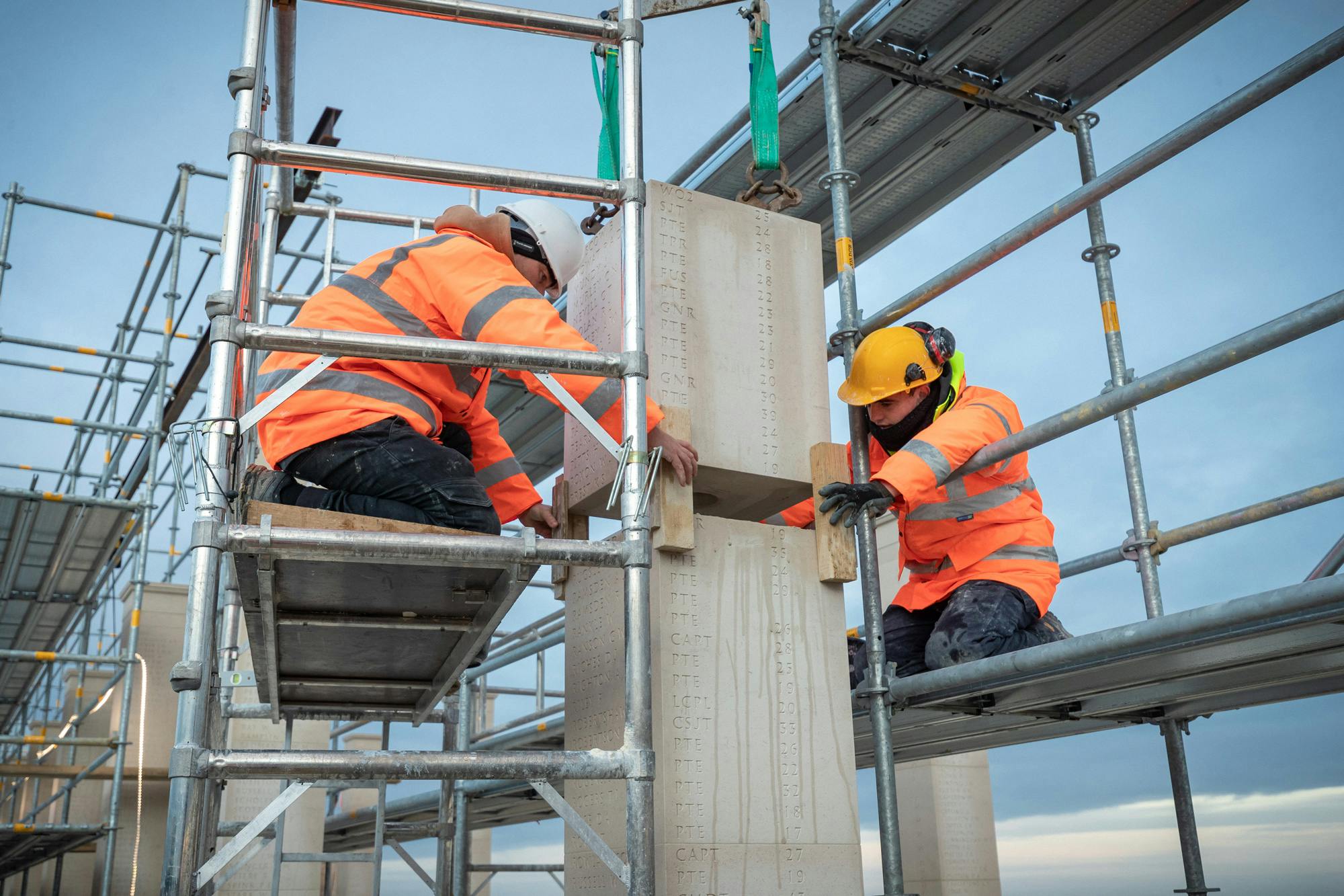Construction workers on scaffolding lay stone blocks to make a column