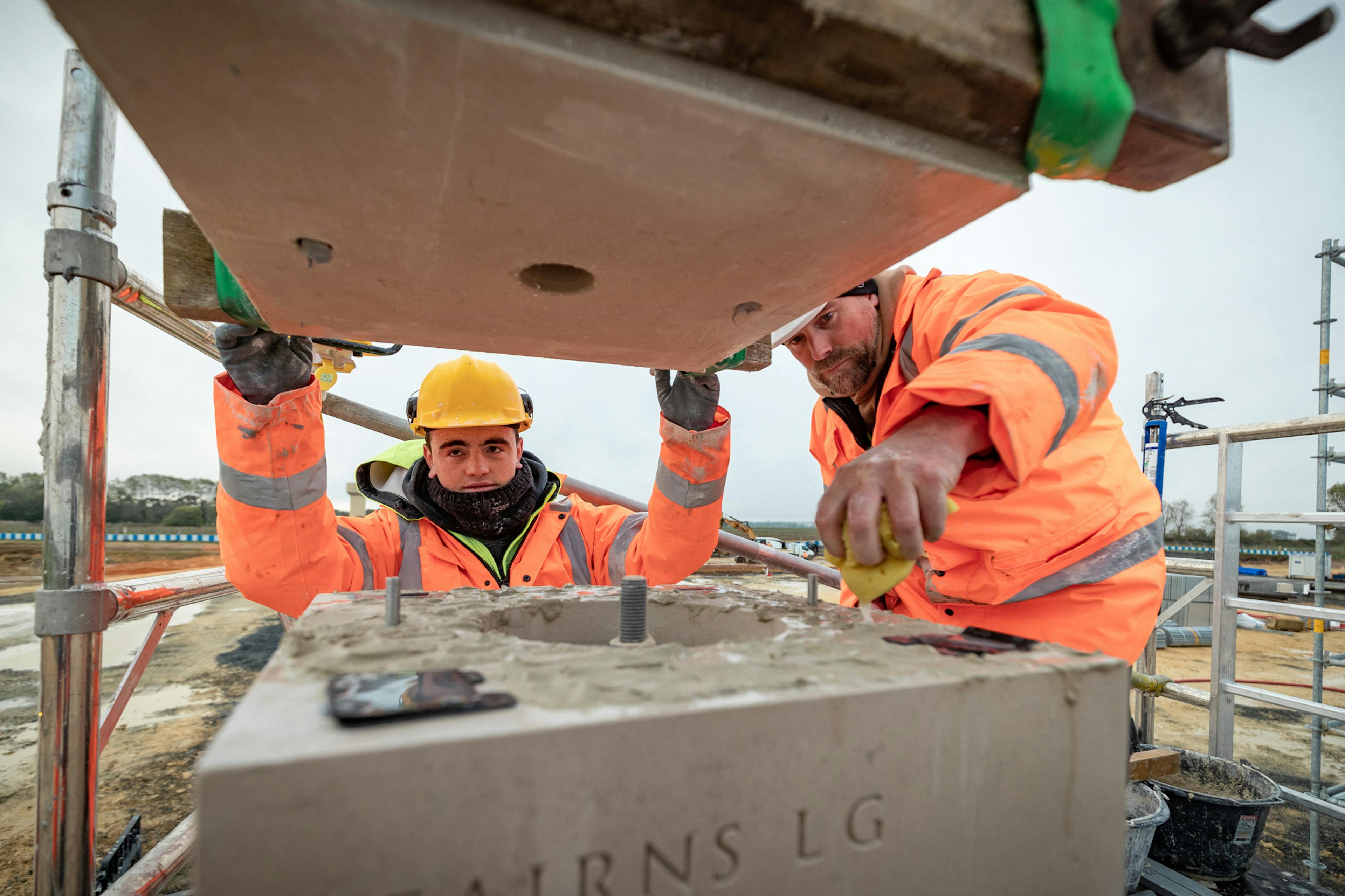 Construction workers on scaffolding lay stone blocks to make a column