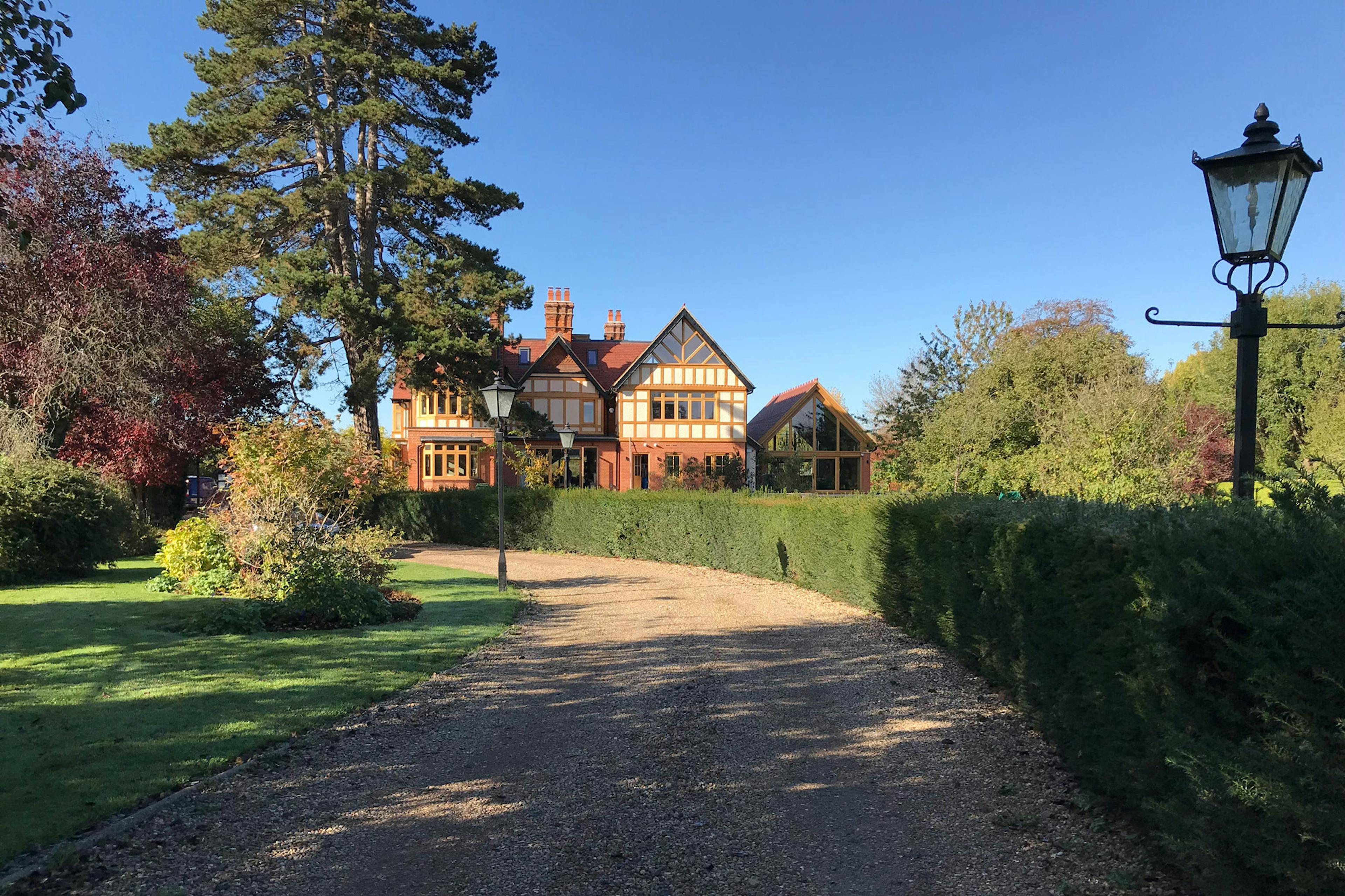 An oak framed extension with a glazed gable end to an arts and craft style house with a driveway and large garden in front