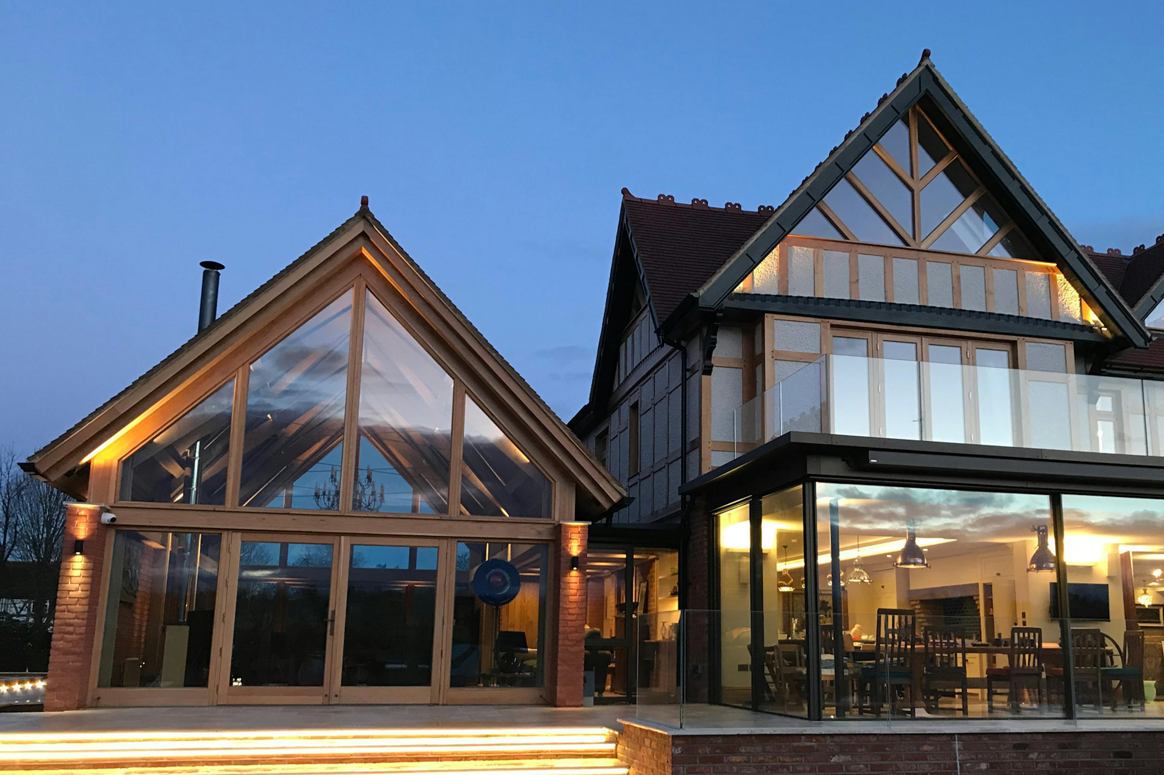 At dusk an oak framed extension with a glazed gable end to an arts and craft style house