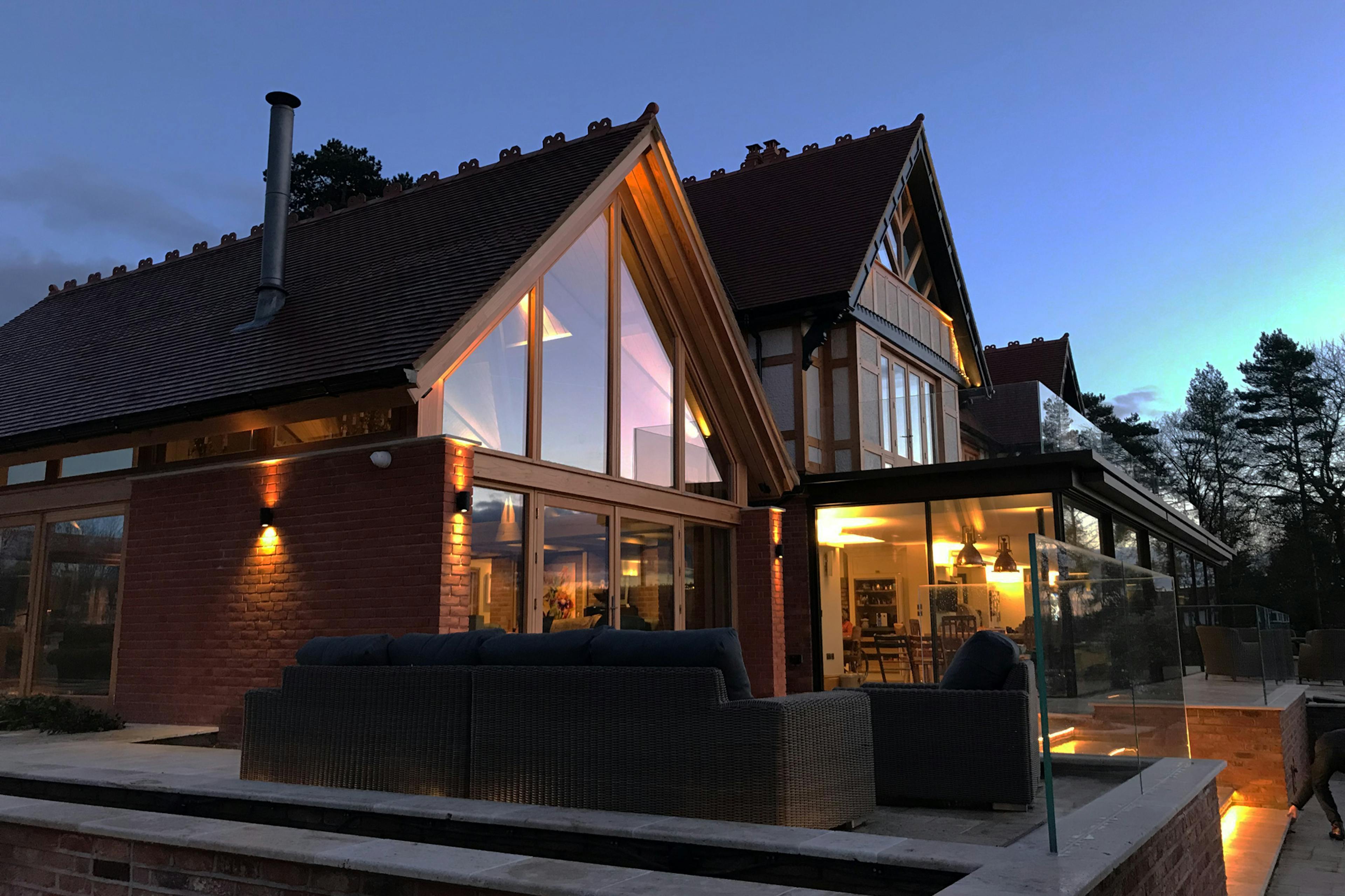 At dusk an oak framed extension with a glazed gable end to an arts and craft style house