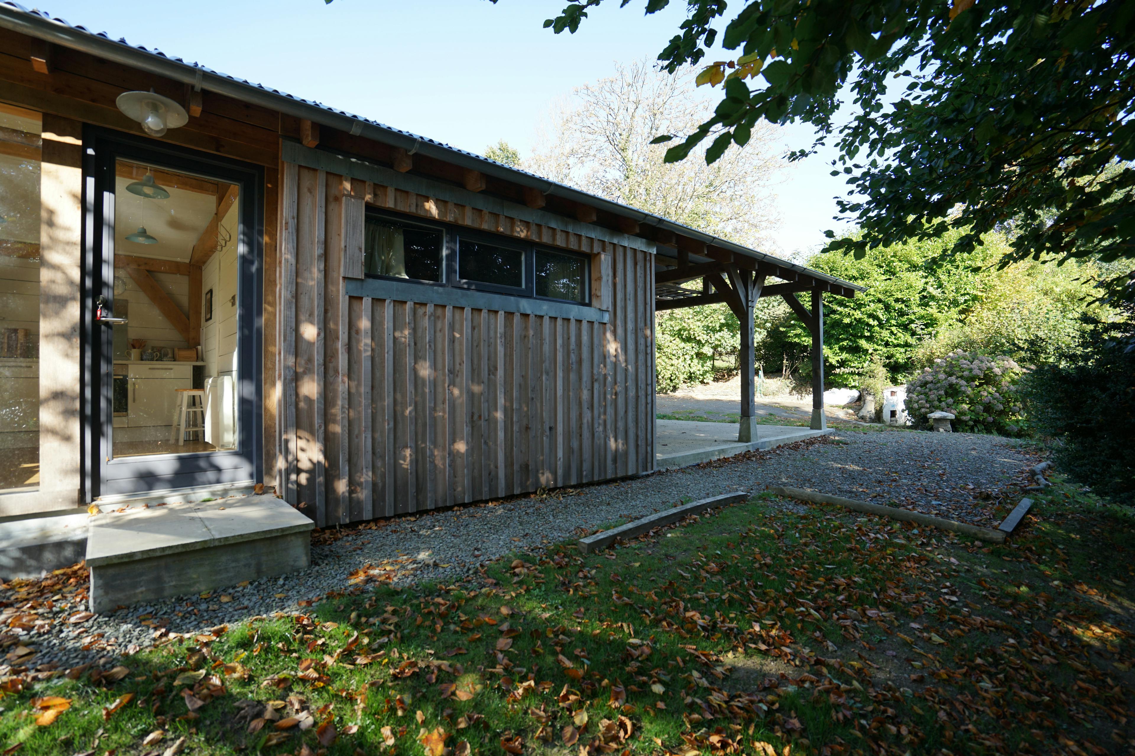 The side of an oak framed cabin showing a front door and rear car port