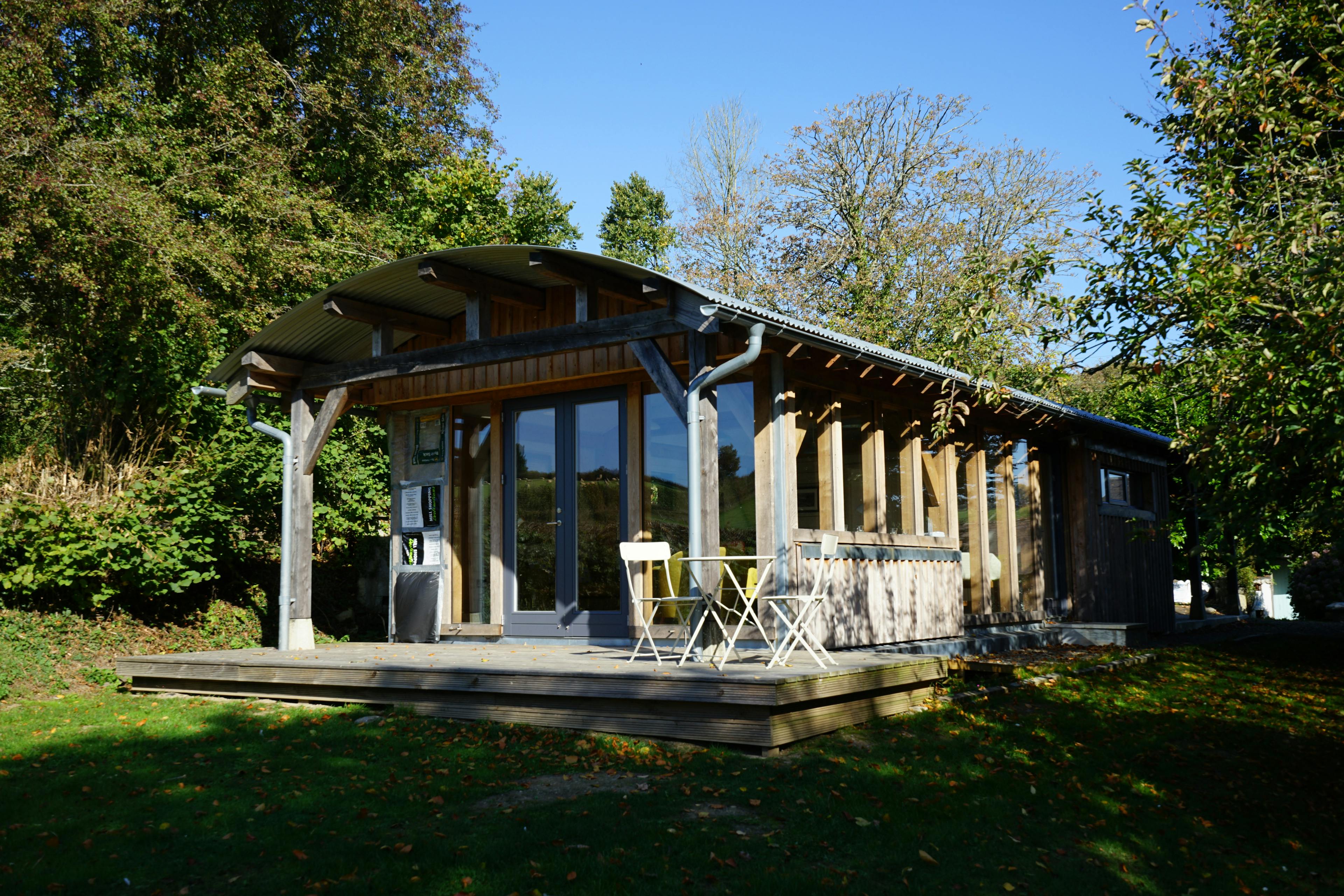 An oak framed cabin with a curved roof corrugated roof and wooden decking with outdoor table and chairs