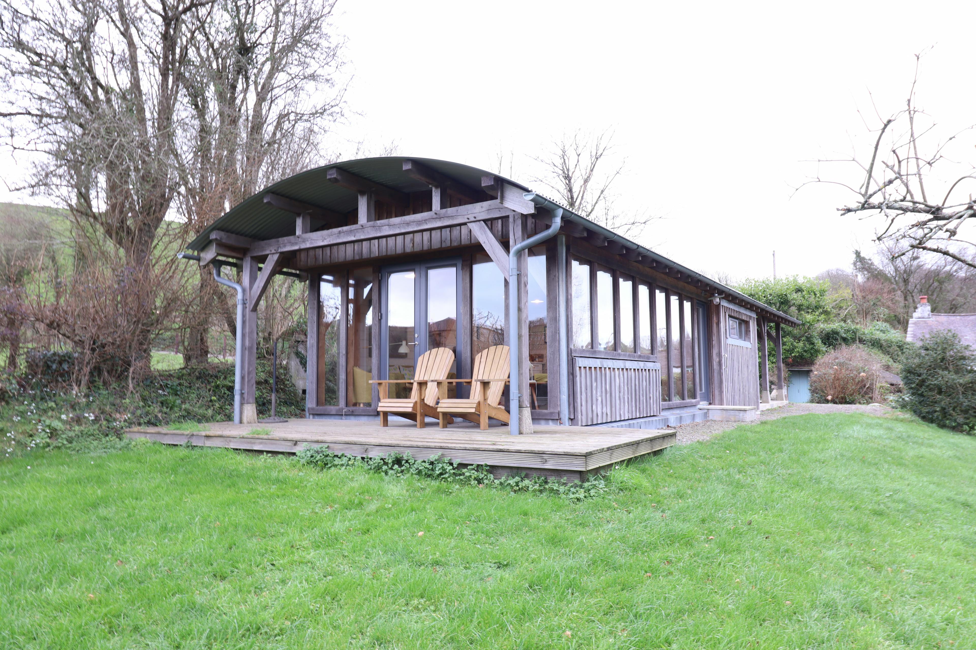 An oak framed cabin with a curved roof corrugated roof and wooden decking with outdoor table and chairs