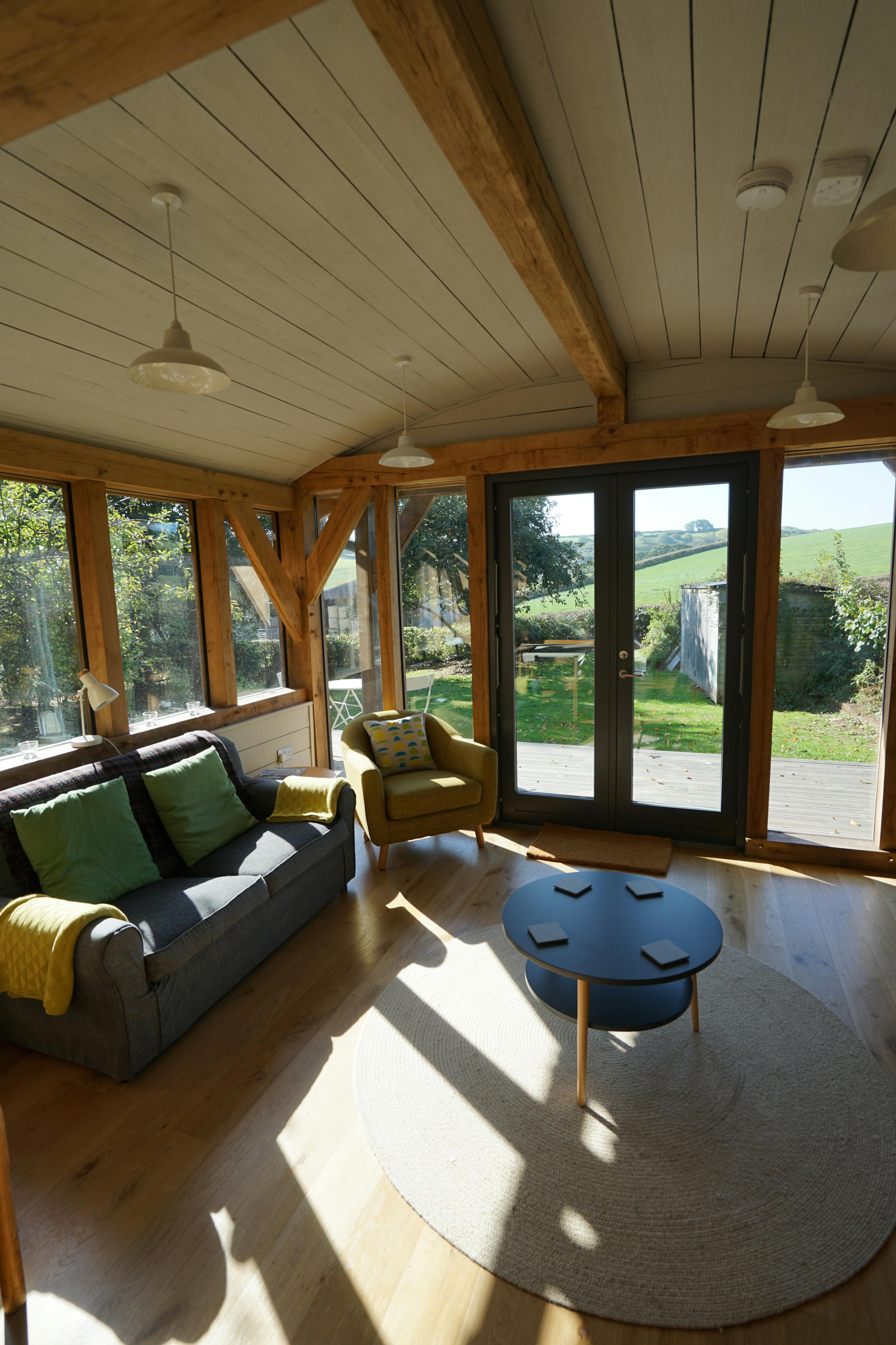 A sofa in the corner of an oak framed cabin with a curved white painted roof
