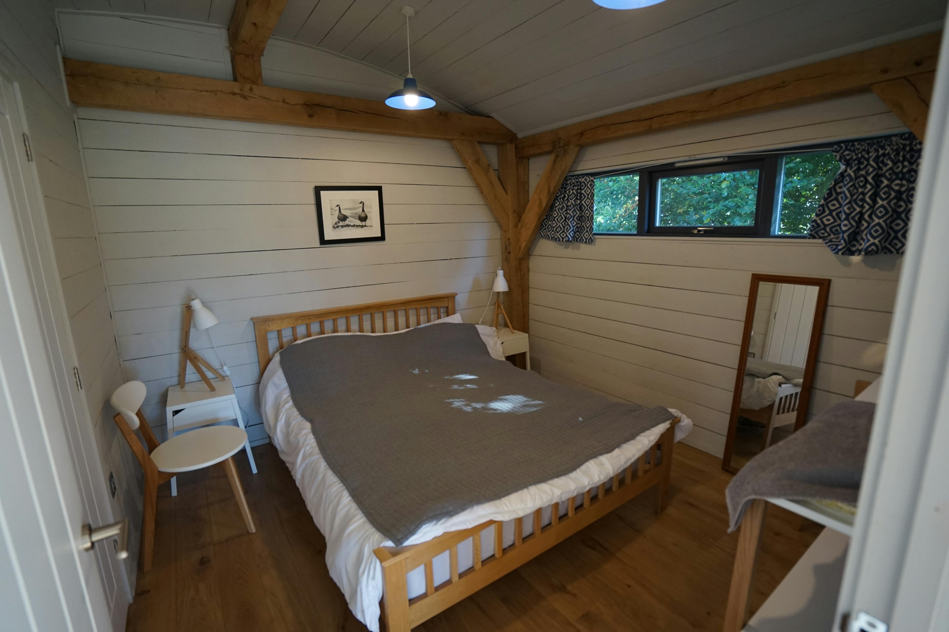 The bedroom of an oak framed cabin with a curved white painted roof