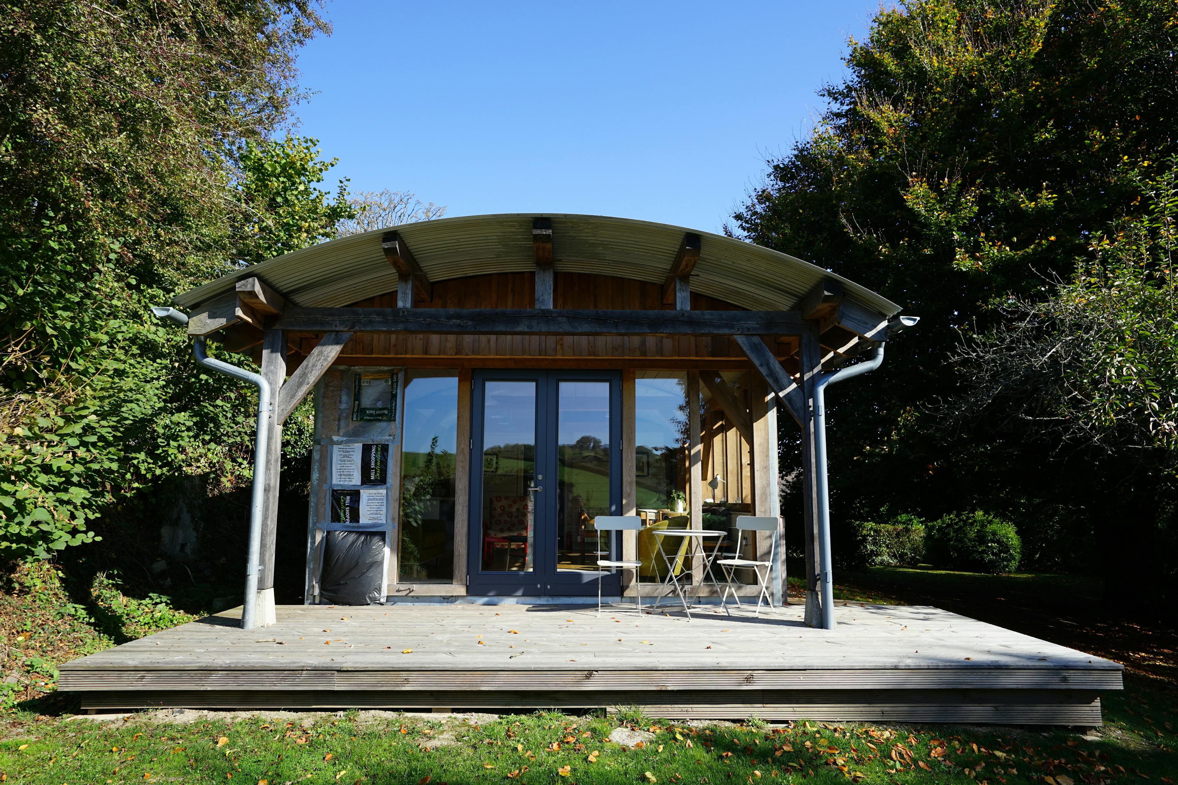 The front of an oak framed cabin with glazed doors, wooden decking and tables & chairs