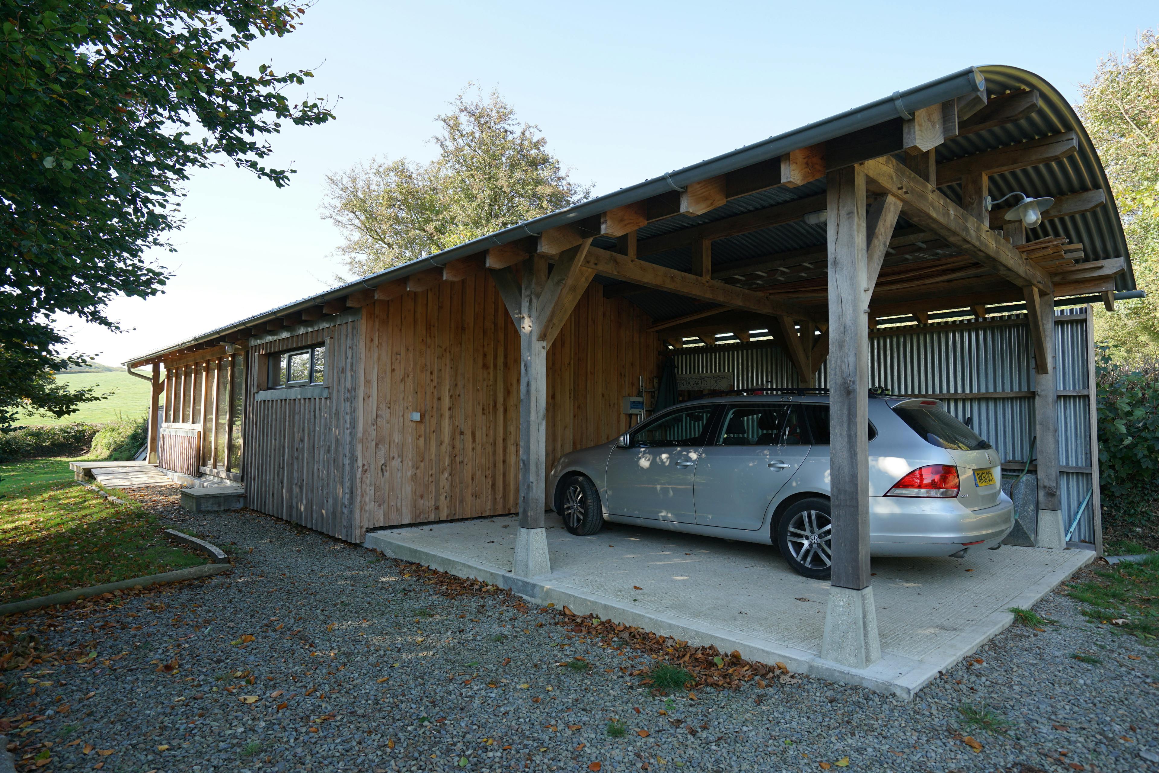 The rear of an oak framed cabin with a curved corrugated roof and a car port