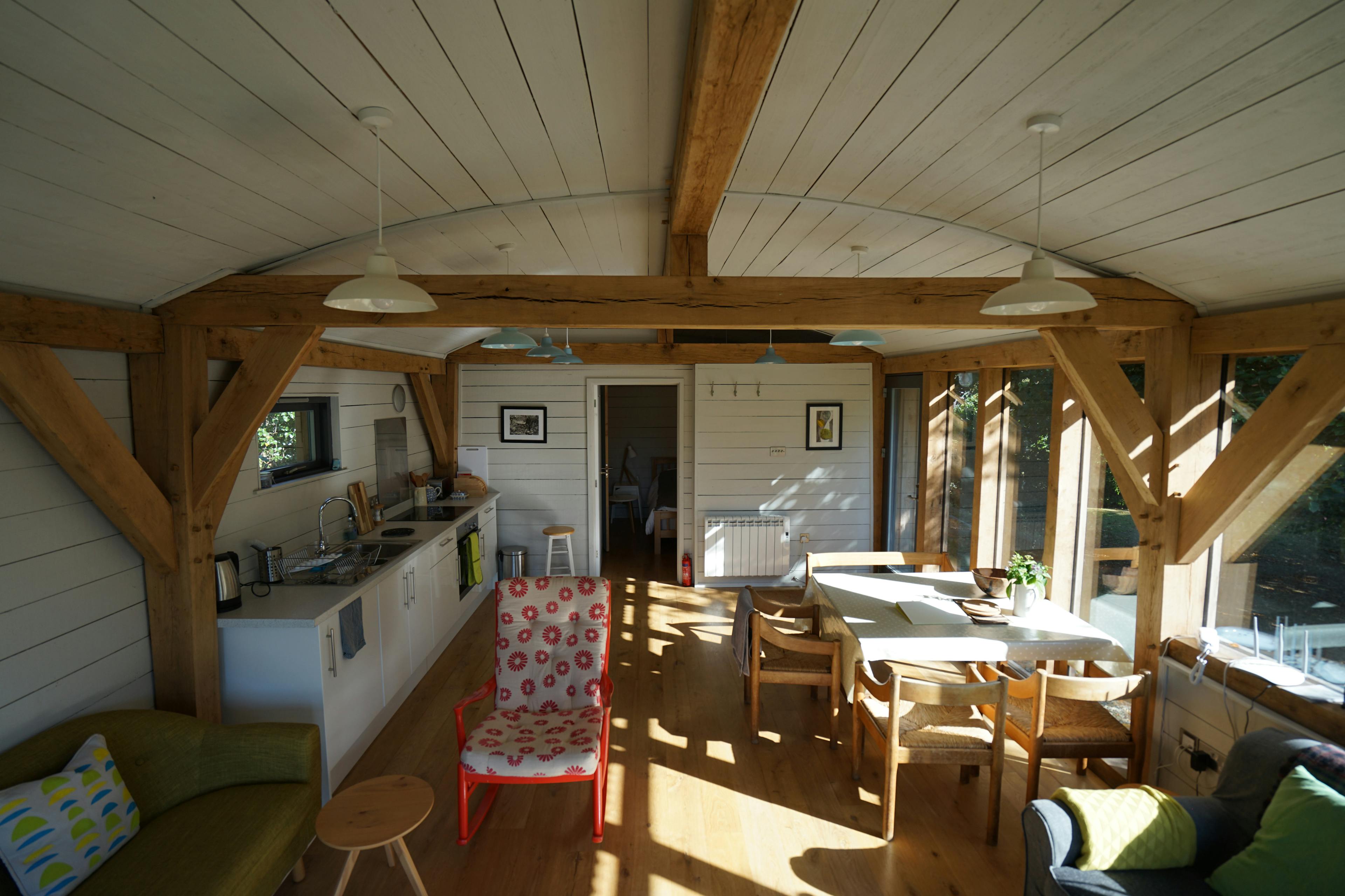 The open plan living, dining, sitting room and kitchen of an oak framed cabin with a curved white painted roof