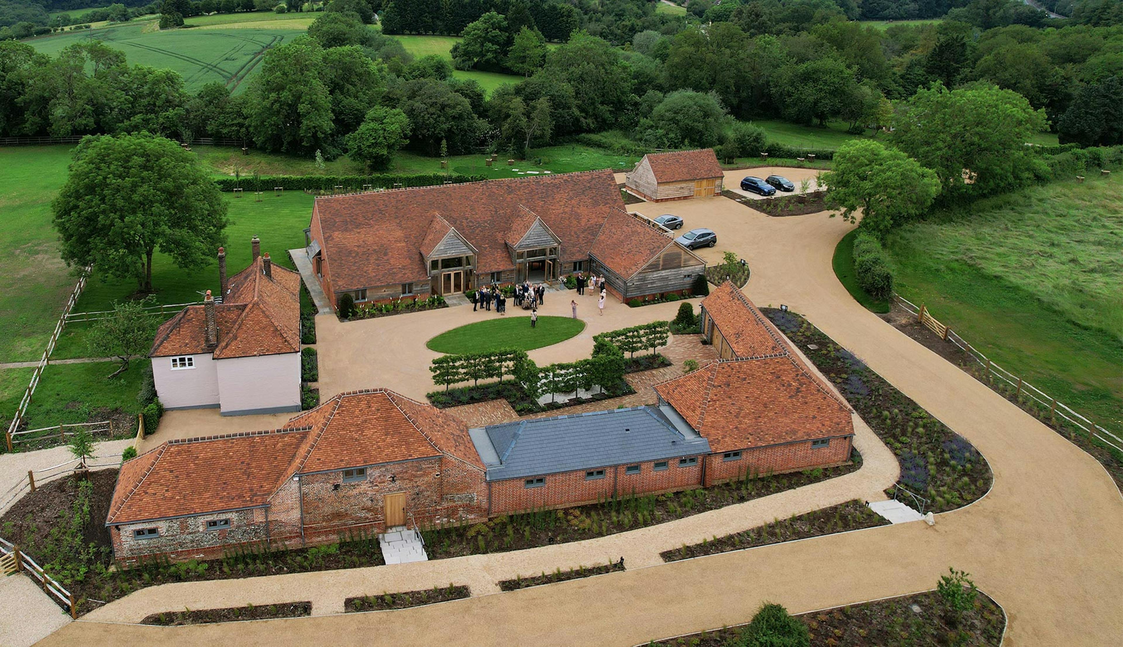 A complex of red tiled buildings on a wedding venue estate surrounding by green trees and fields
