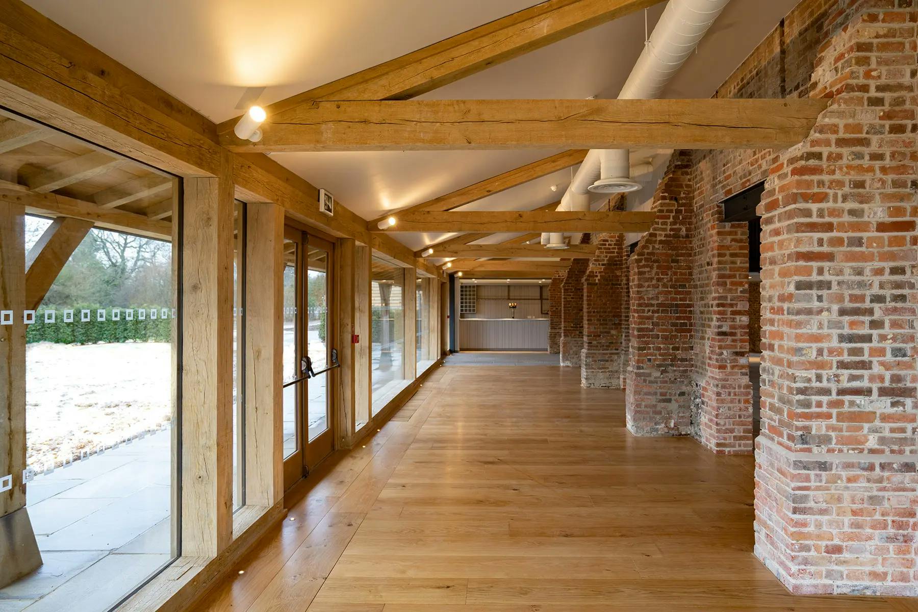 An oak framed wedding barn hall with a red brick wall and glazing with an oak frame veranda outside