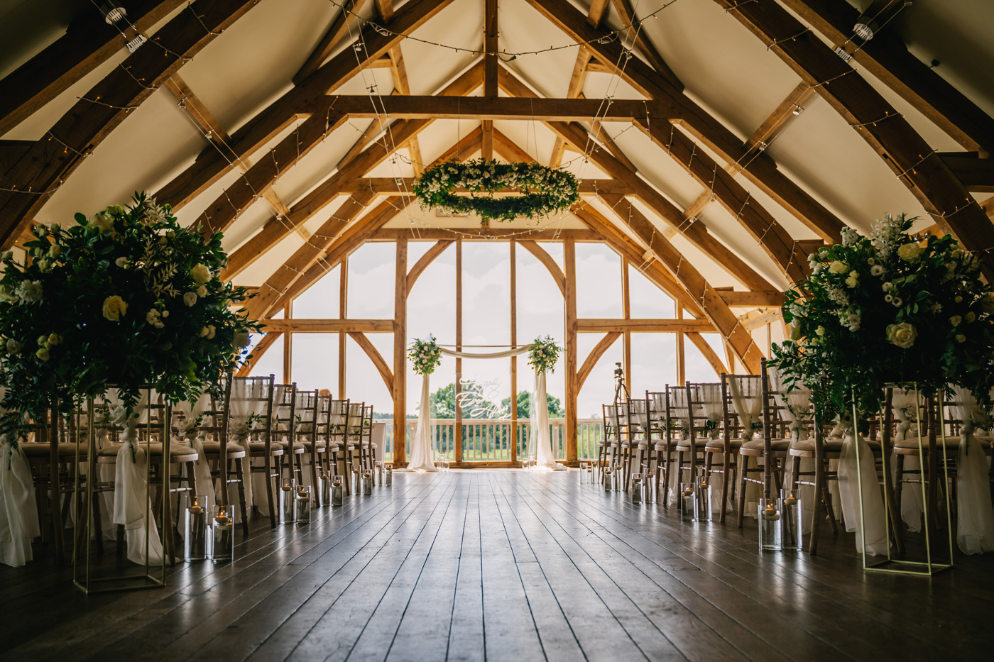 An oak framed wedding barn is ready for a wedding ceremony with rows of chairs and flowers