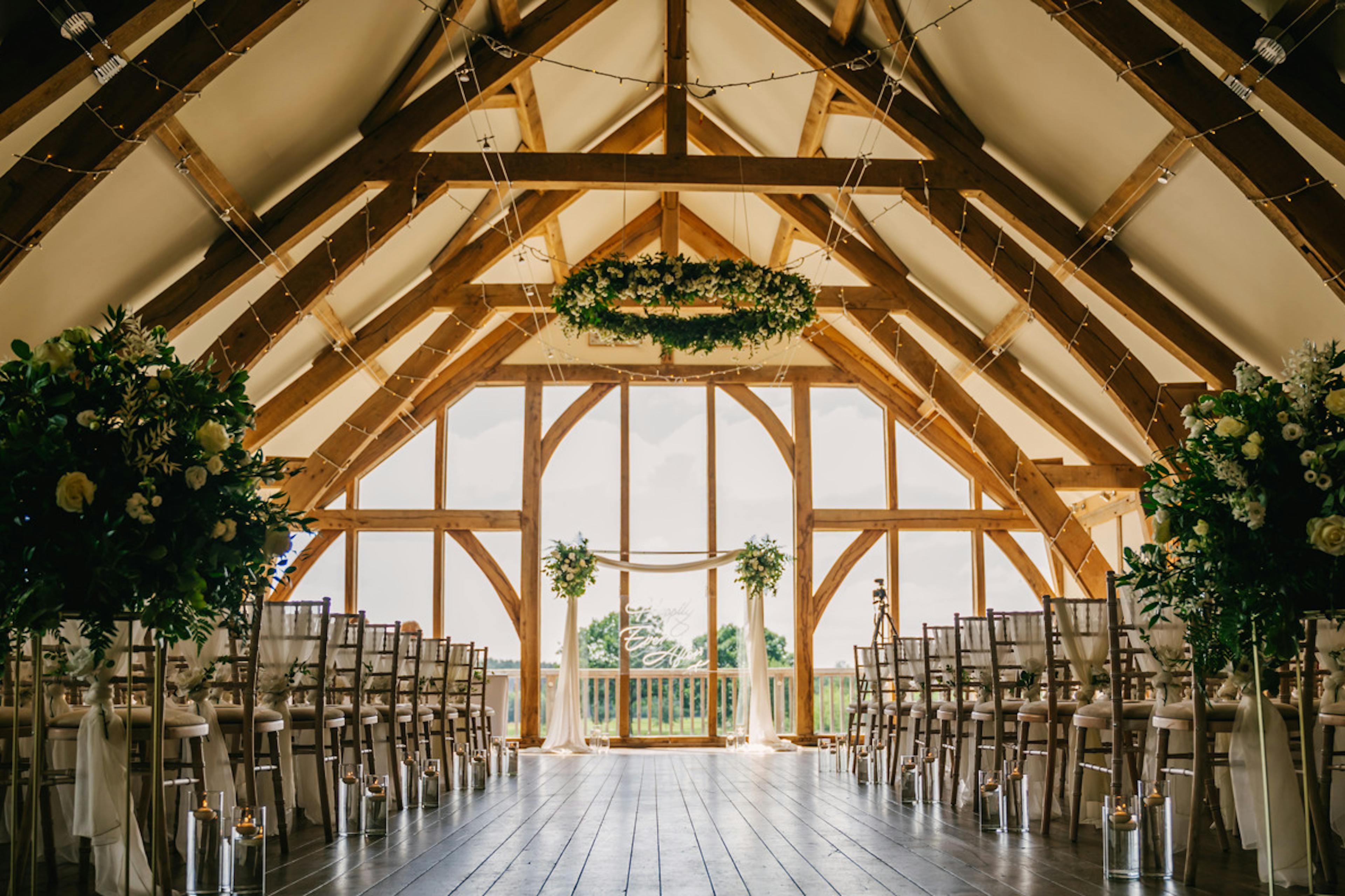 An oak framed wedding barn is ready for a wedding ceremony with rows of chairs and flowers