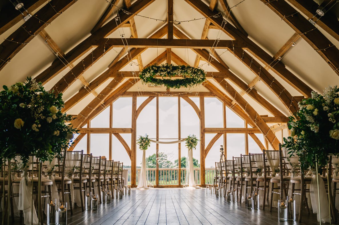 An oak framed wedding barn is ready for a wedding ceremony with rows of chairs and flowers