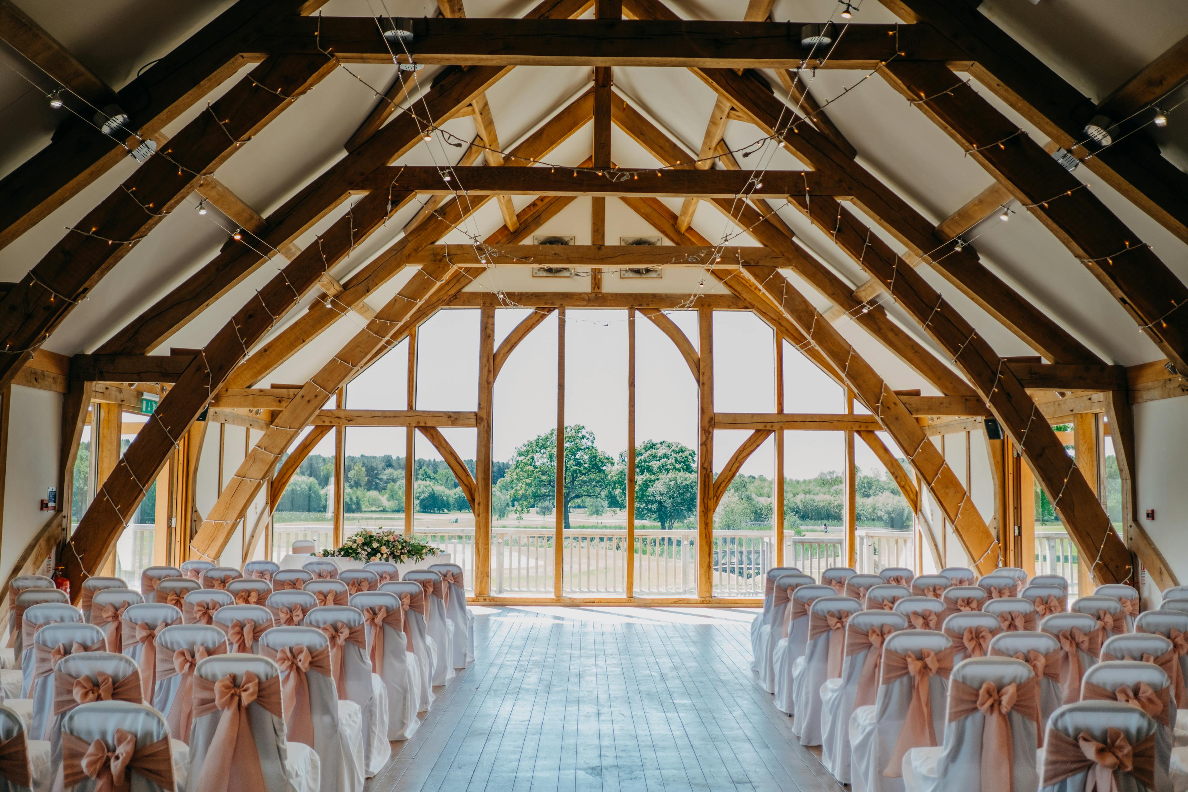 An oak framed wedding barn is ready for a wedding ceremony with rows of chairs and flowers