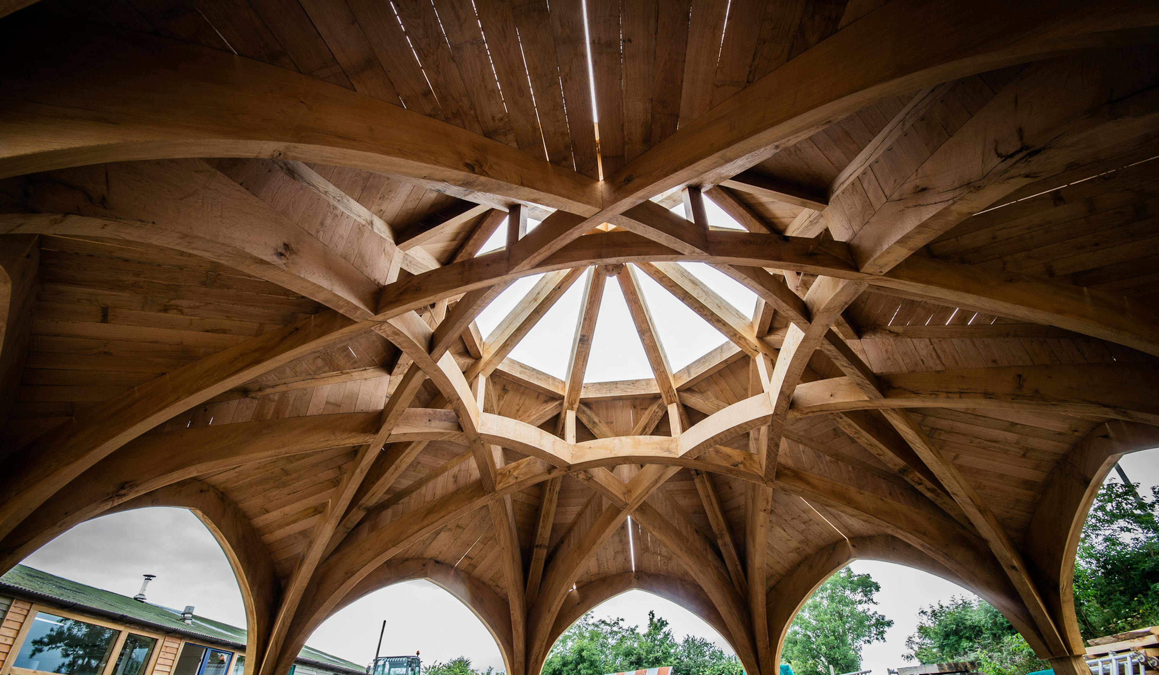 The underneath of a complex octagonal oak roof structure outside some workshops in a carpentry yard