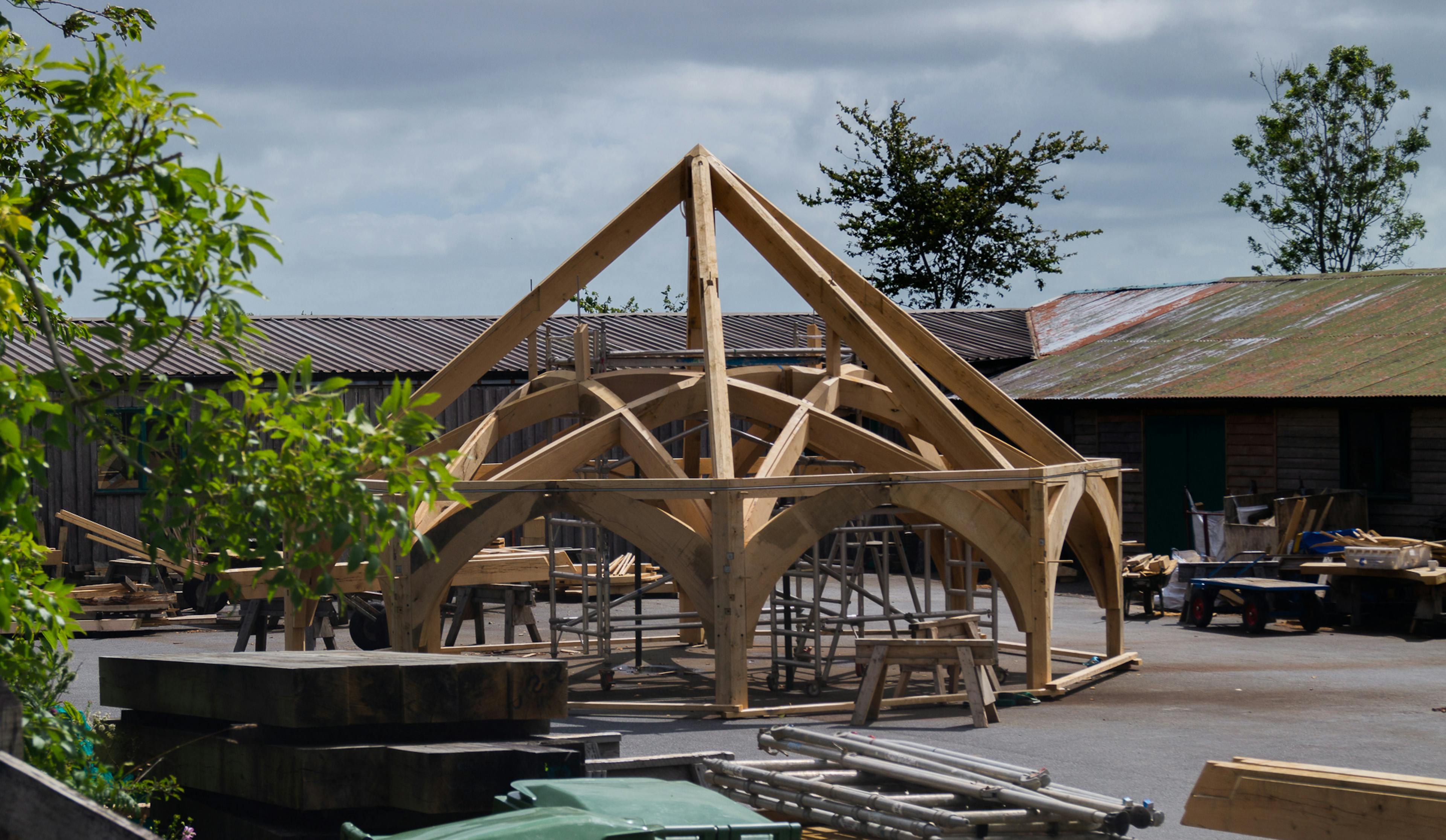 A complex octagonal oak roof structure outside some workshops in a carpentry yard